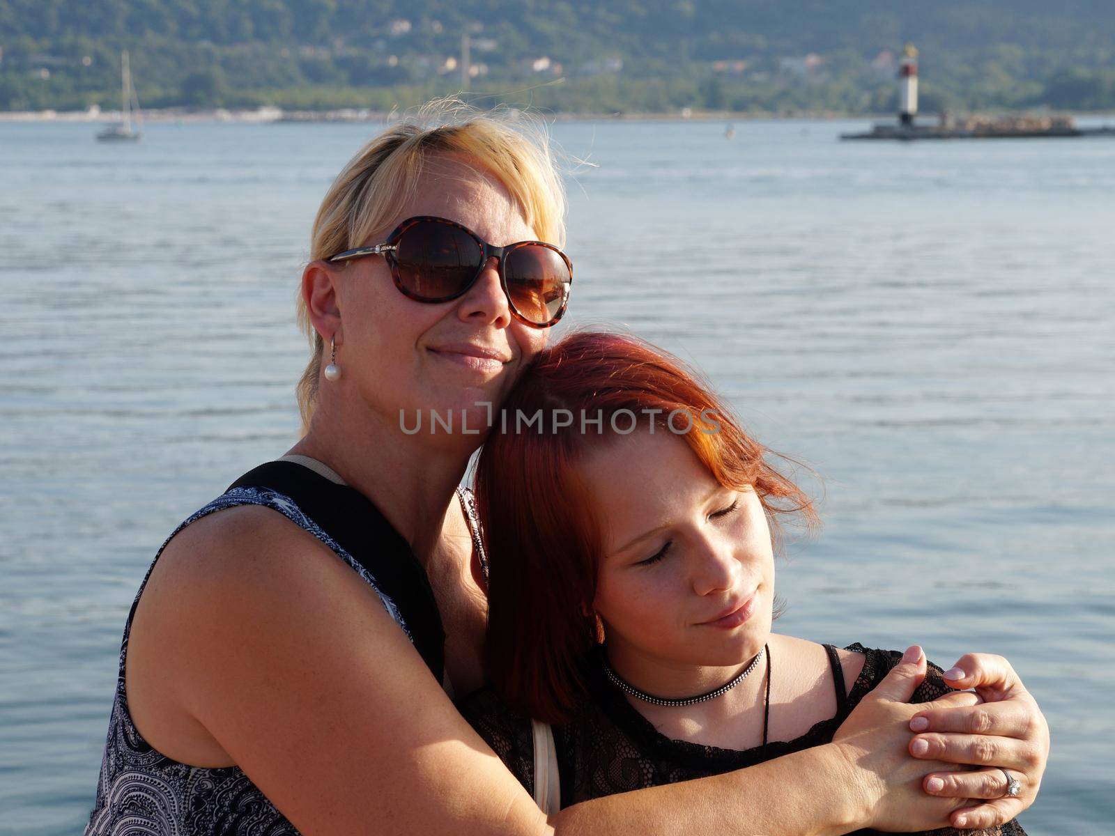 mother hugging a teenage girl against the backdrop of the sea in sunlight, portrait