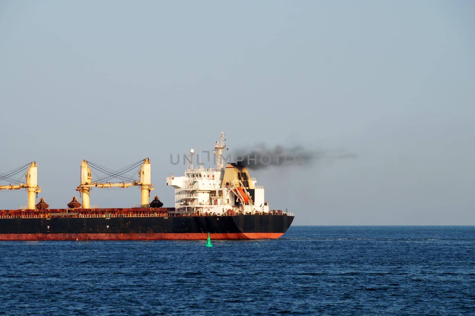 Cargo ship with black smoke from the chimney on the sea horizon close-up