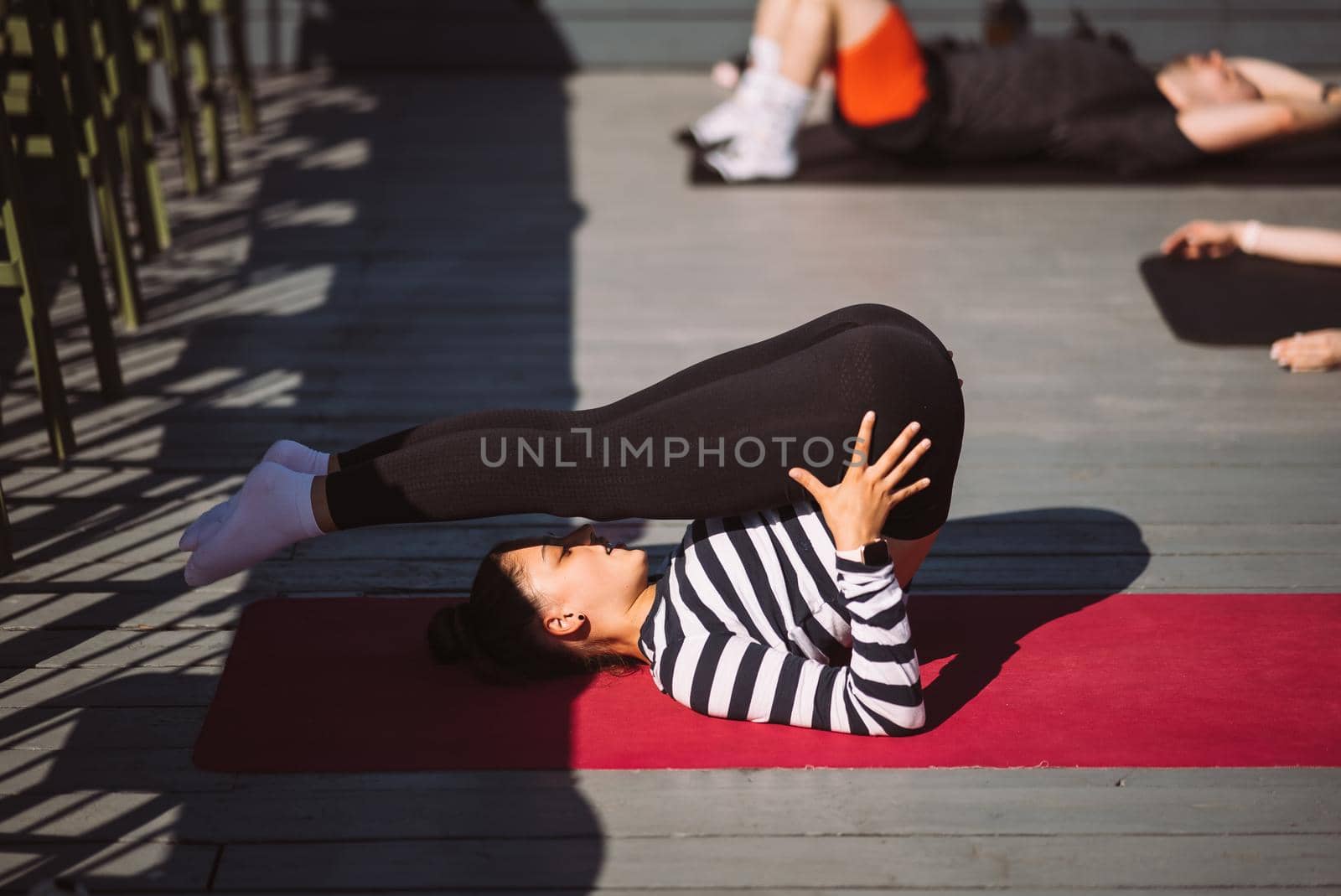 Yogi woman and diverse group of young sporty people practicing yoga, female students training at house's roof. Well being, wellness concept