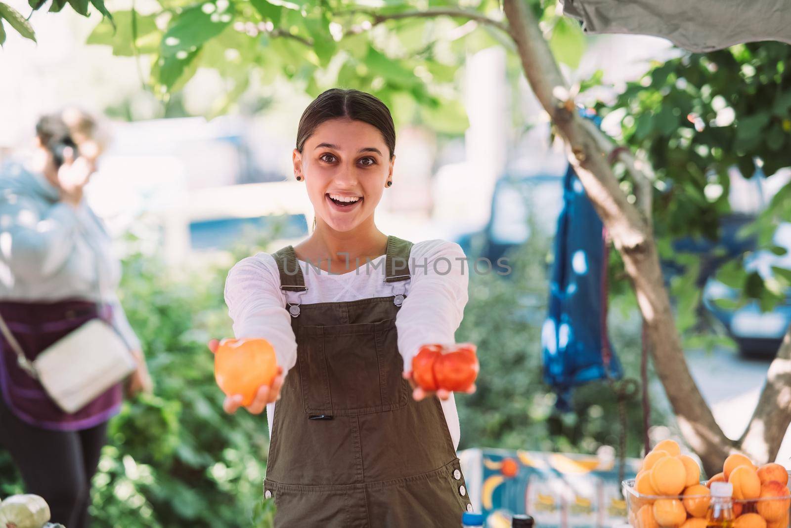 Young positive salesgirl at job, selling sells home-grown vegetables and fruits in vegetable shop