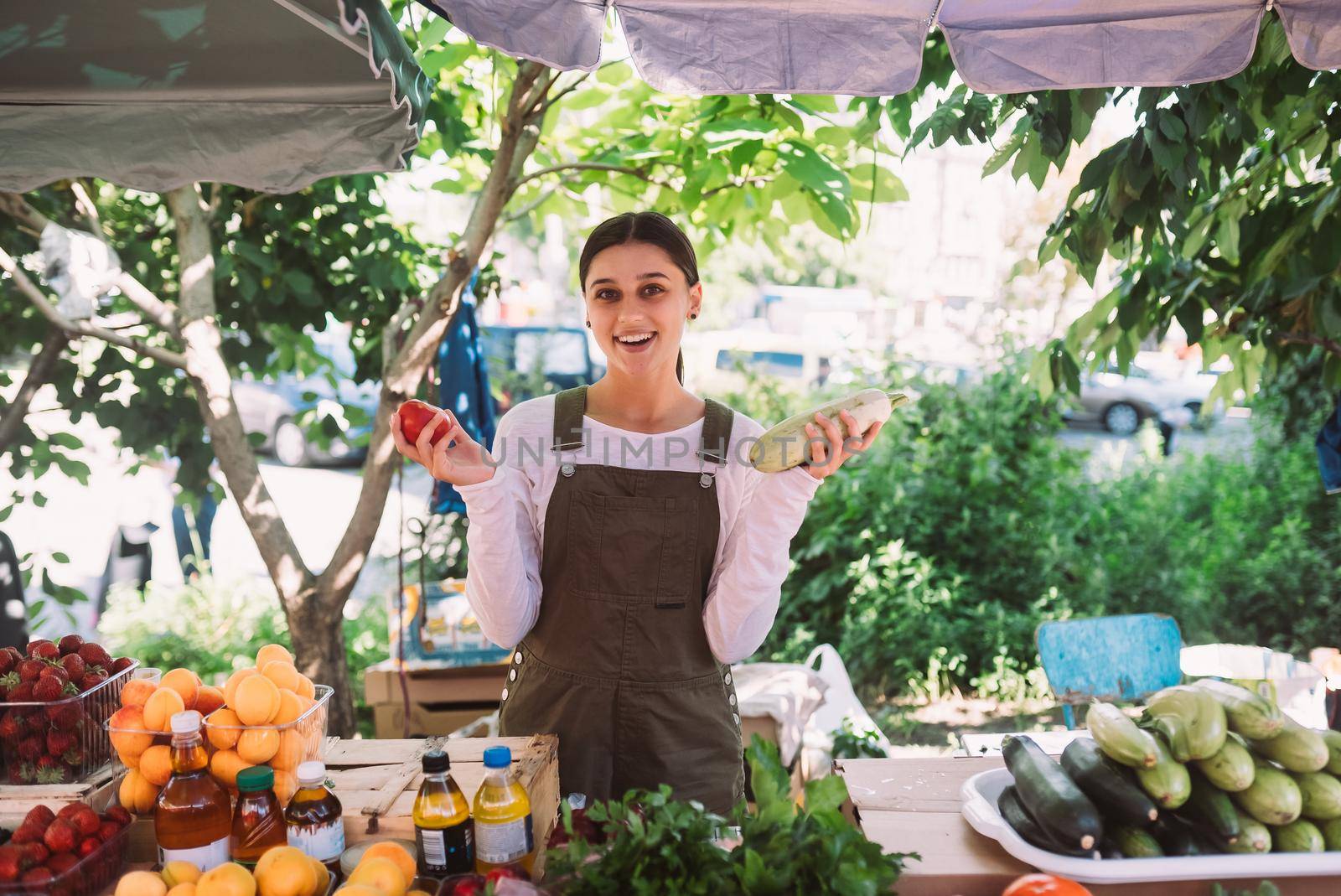 Young positive salesgirl at job, selling sells home-grown vegetables and fruits in vegetable shop