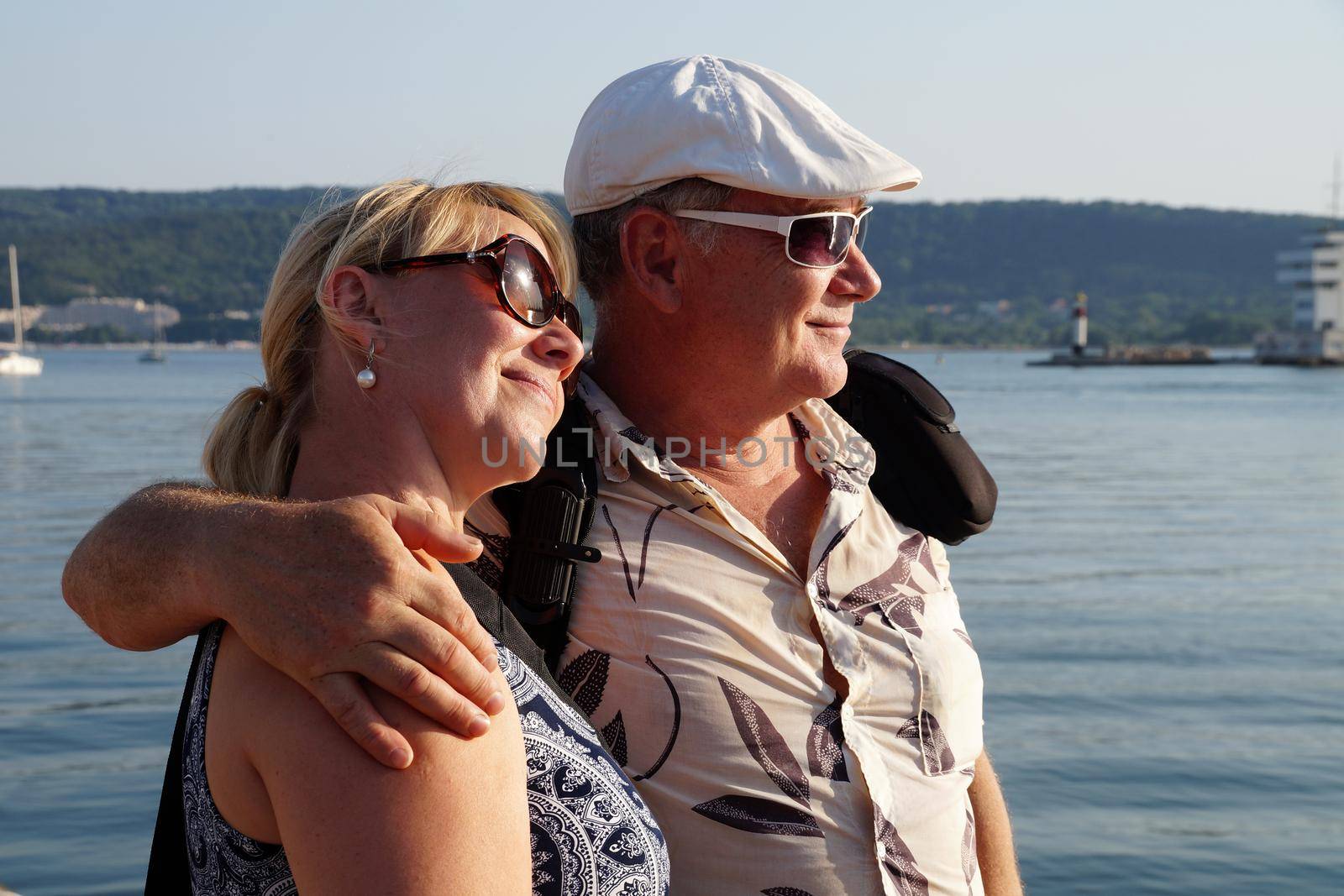 portrait of a smiling middle aged couple in sunglasses on the sea by Annado