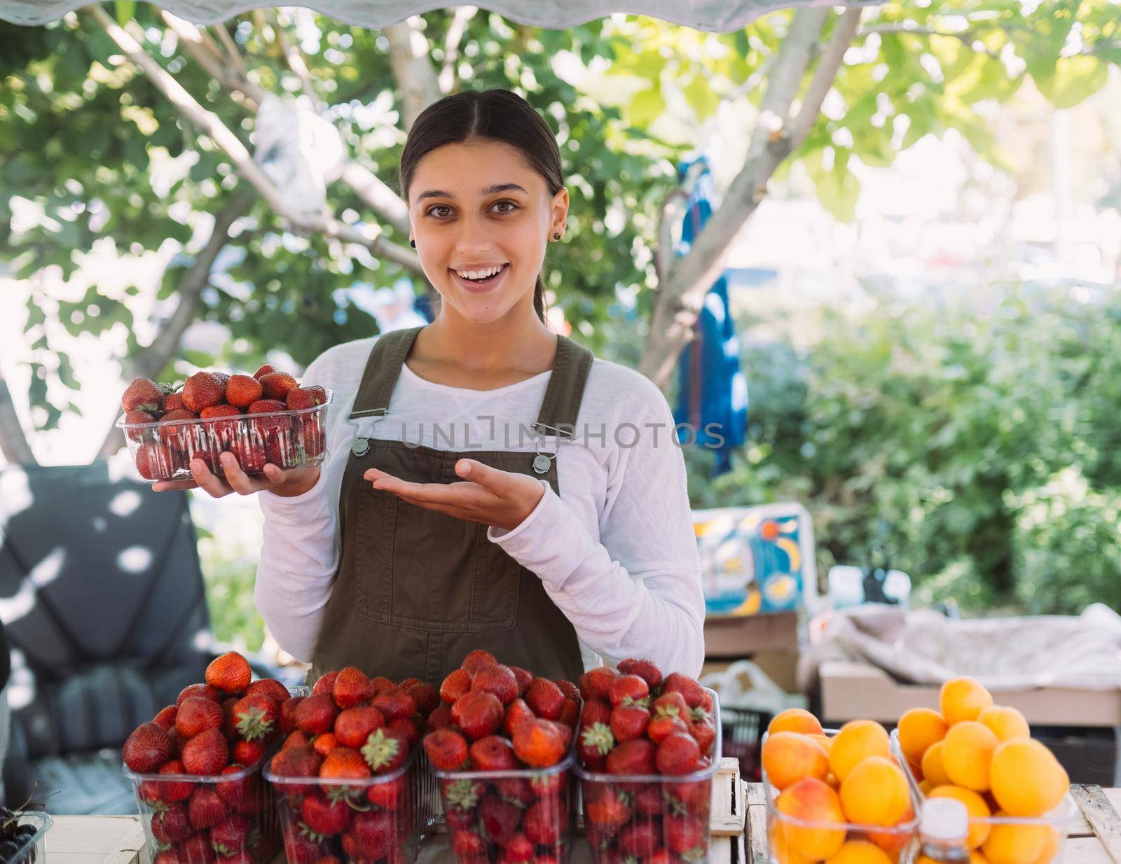 Young positive salesgirl at job, selling sells home-grown vegetables and fruits in vegetable shop