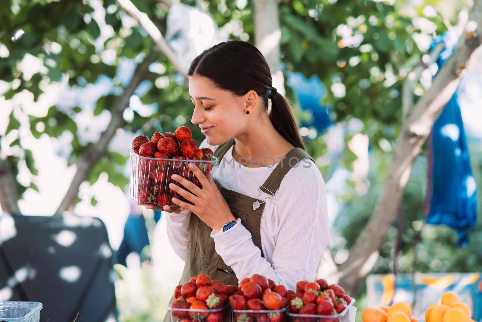 Young positive salesgirl at job, selling sells home-grown vegetables and fruits in vegetable shop