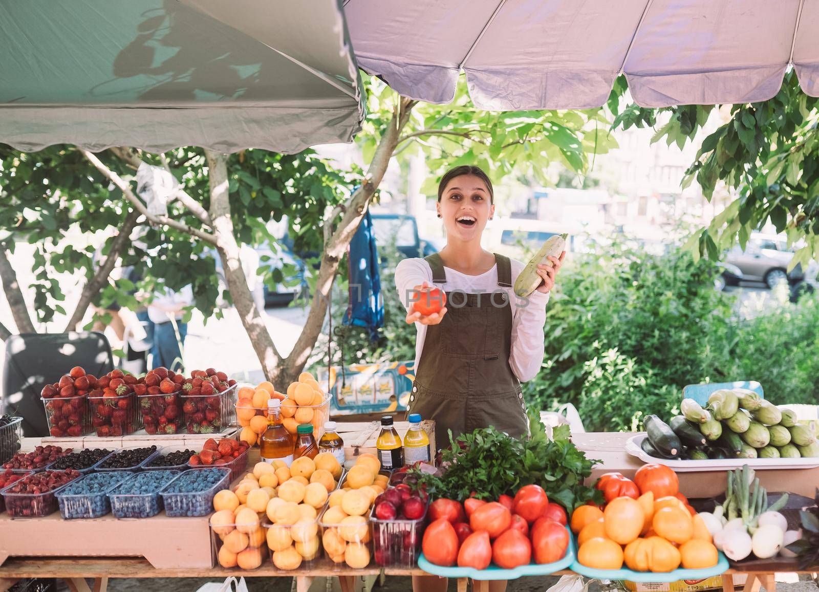 Young positive salesgirl at job, selling sells home-grown vegetables and fruits in vegetable shop
