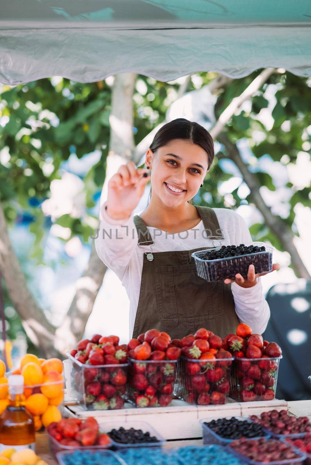 Young positive salesgirl at job, selling sells home-grown vegetables and fruits in vegetable shop