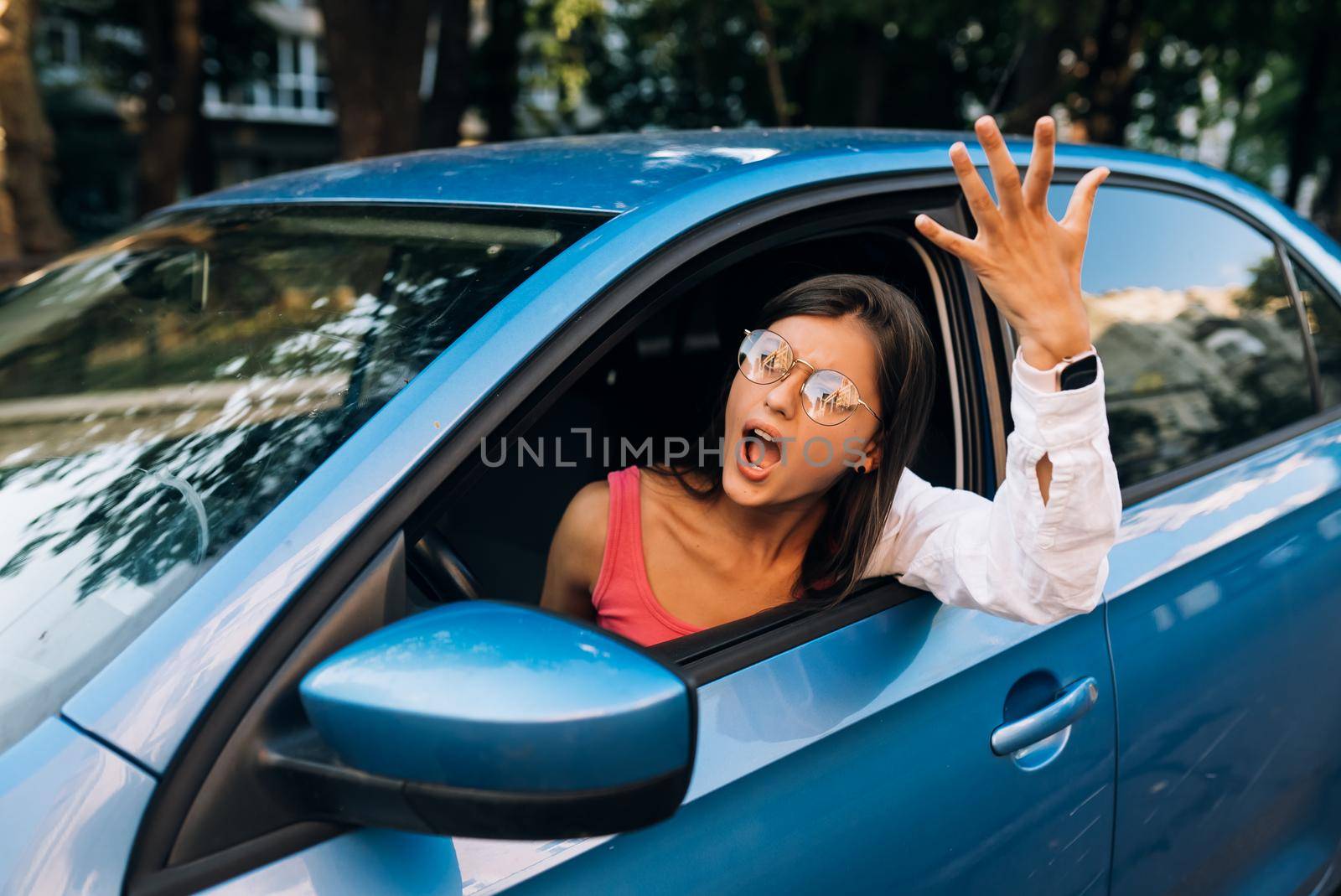 A young angry woman peeks out of the car window. A woman shows her displeasure