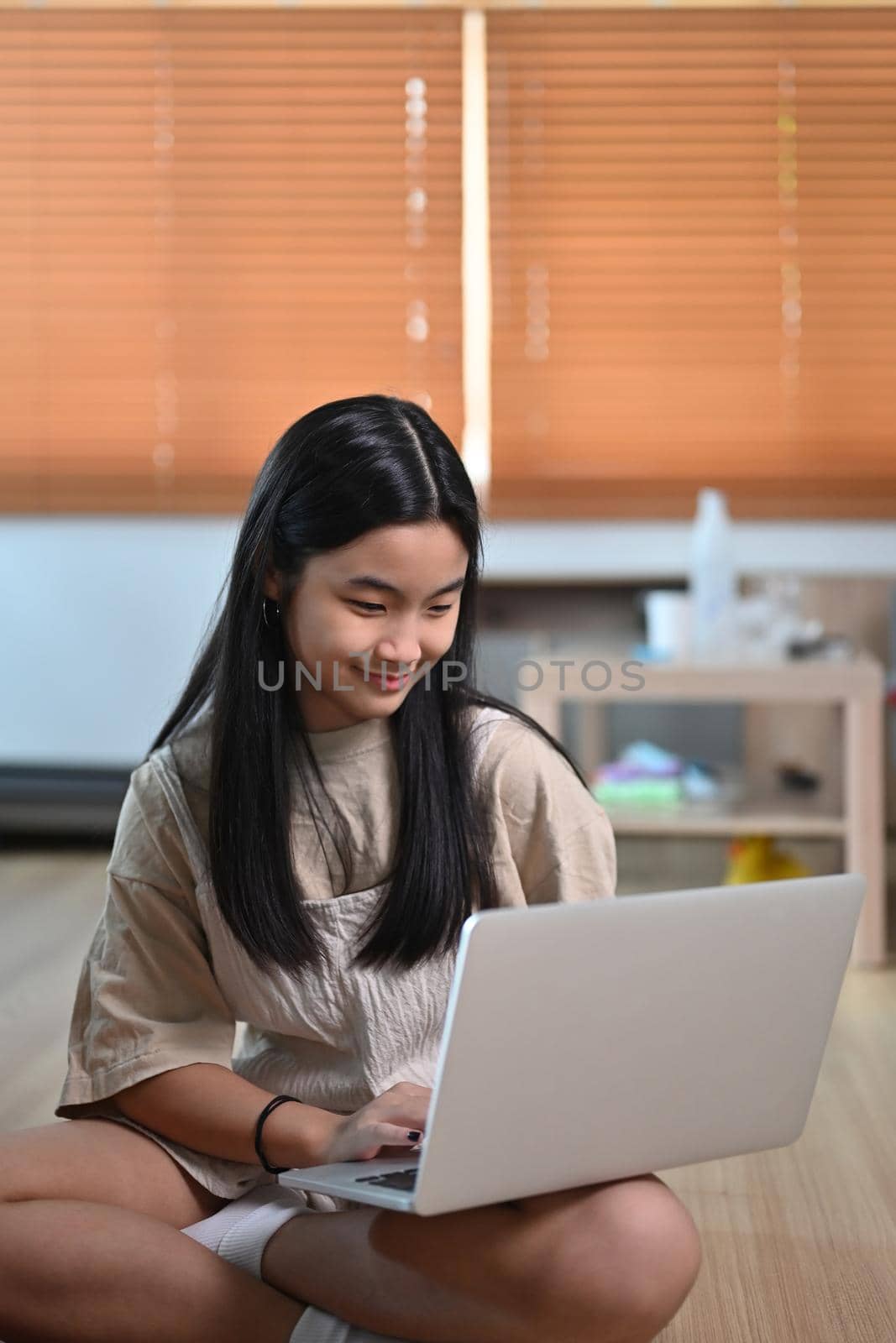 Happy asian girl sitting on floor in living room and using laptop computer. by prathanchorruangsak
