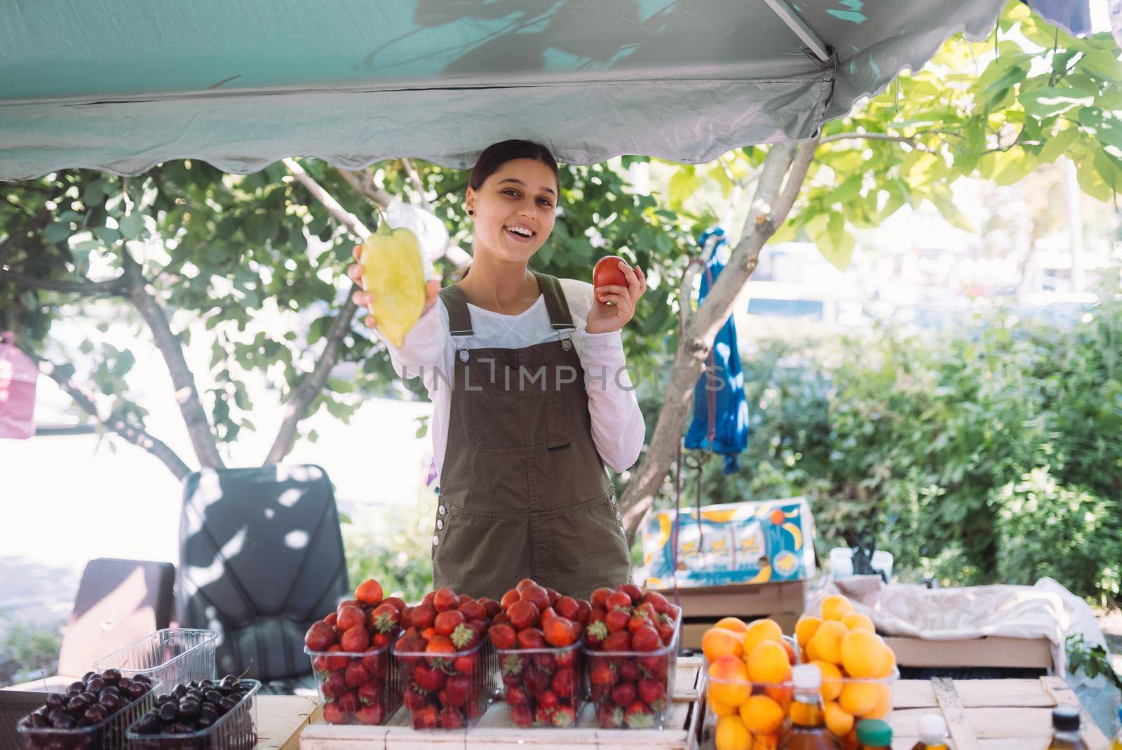 Young positive salesgirl at job, selling sells home-grown vegetables and fruits in vegetable shop