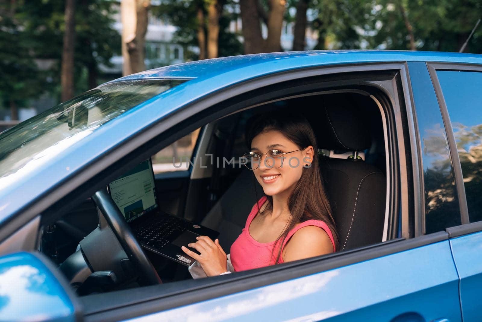 Young woman using laptop in her car while driving. Safe driving concept
