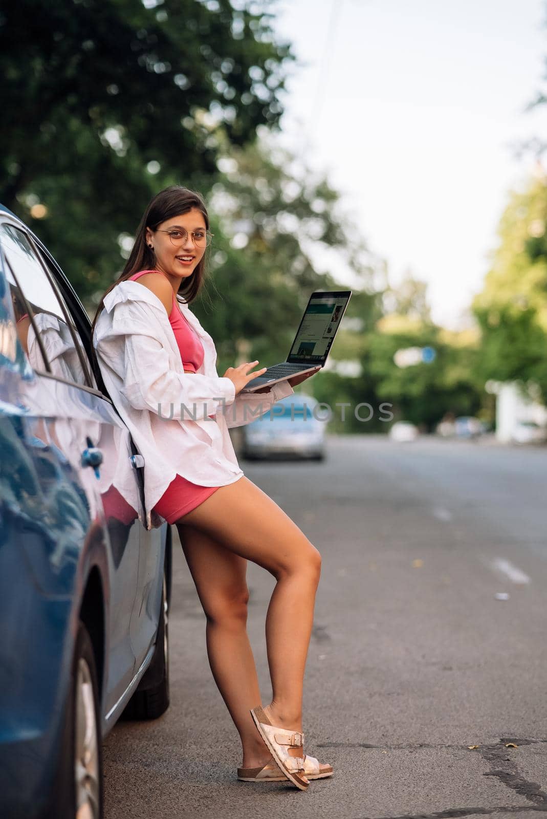 A young woman uses a laptop near a car in city center outdoors