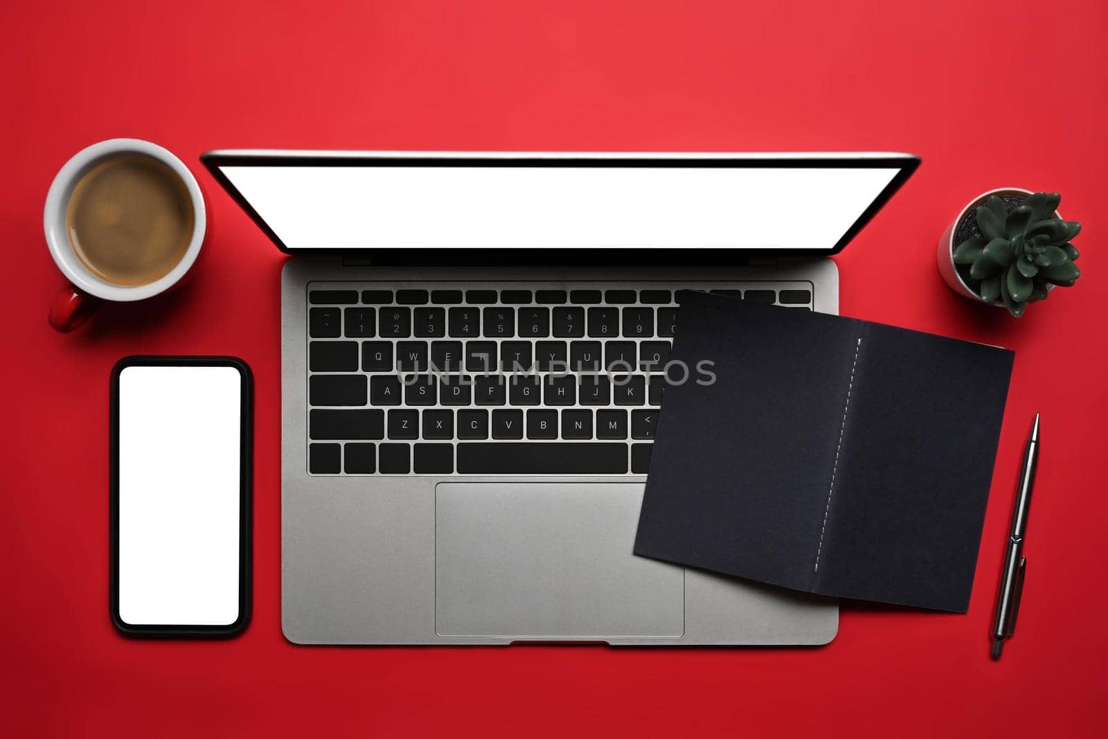 Above view laptop computer, smart phone, coffee cup and notebook on red background.