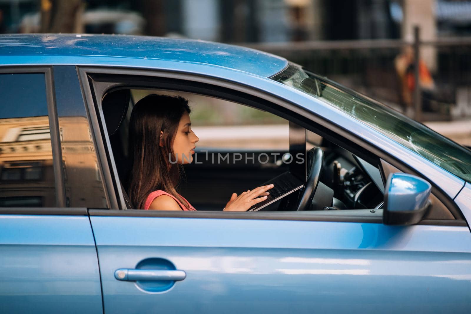Young woman using laptop in her car while driving. Safe driving concept