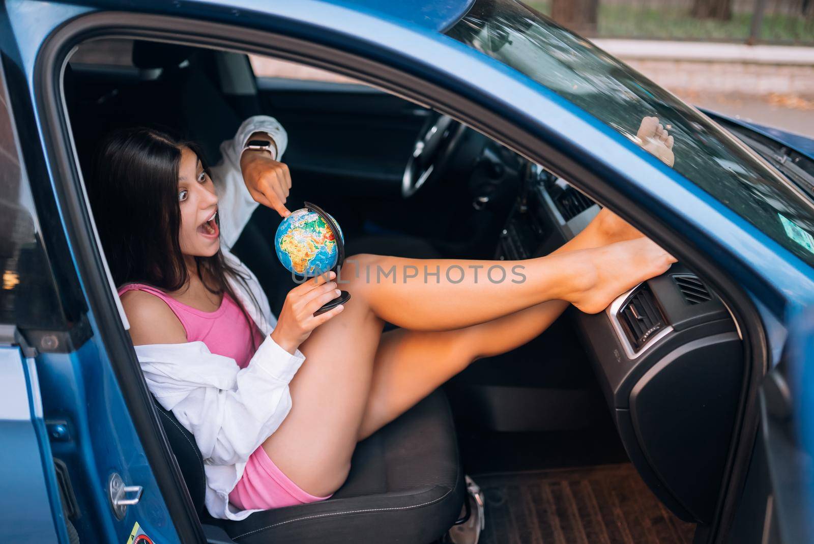 Young woman sitting in a car and holding a globe, travel concept