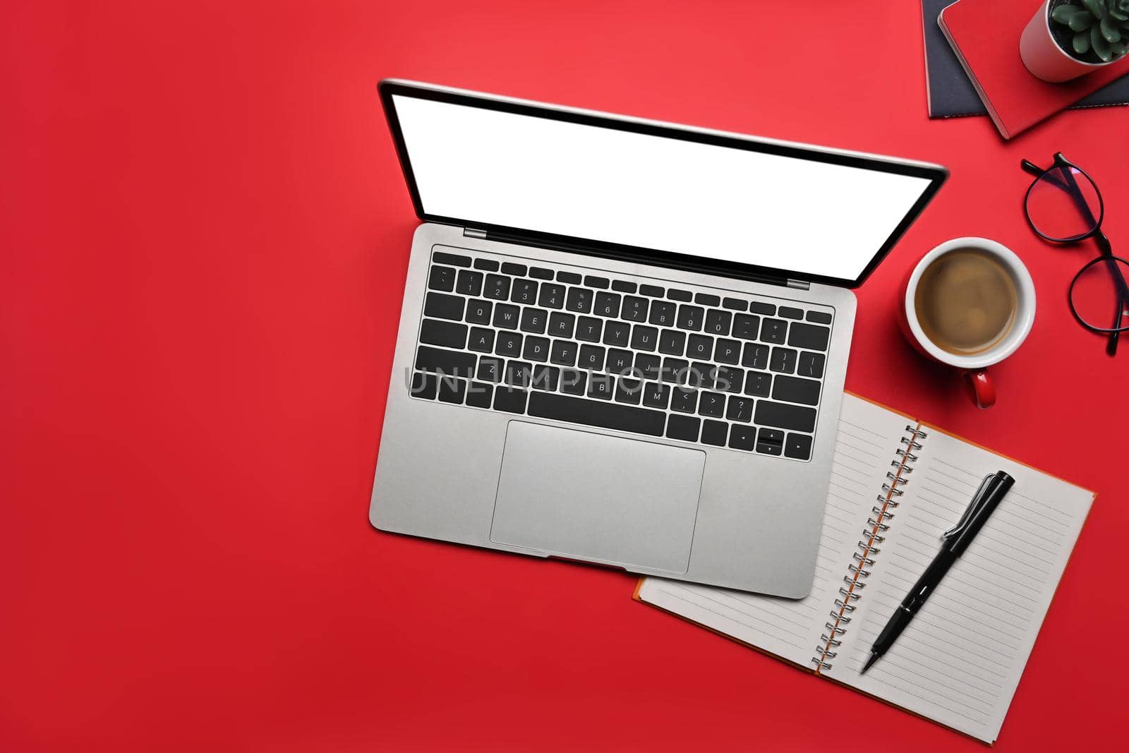 Computer laptop with white screen, notebook and coffee cup on red background.