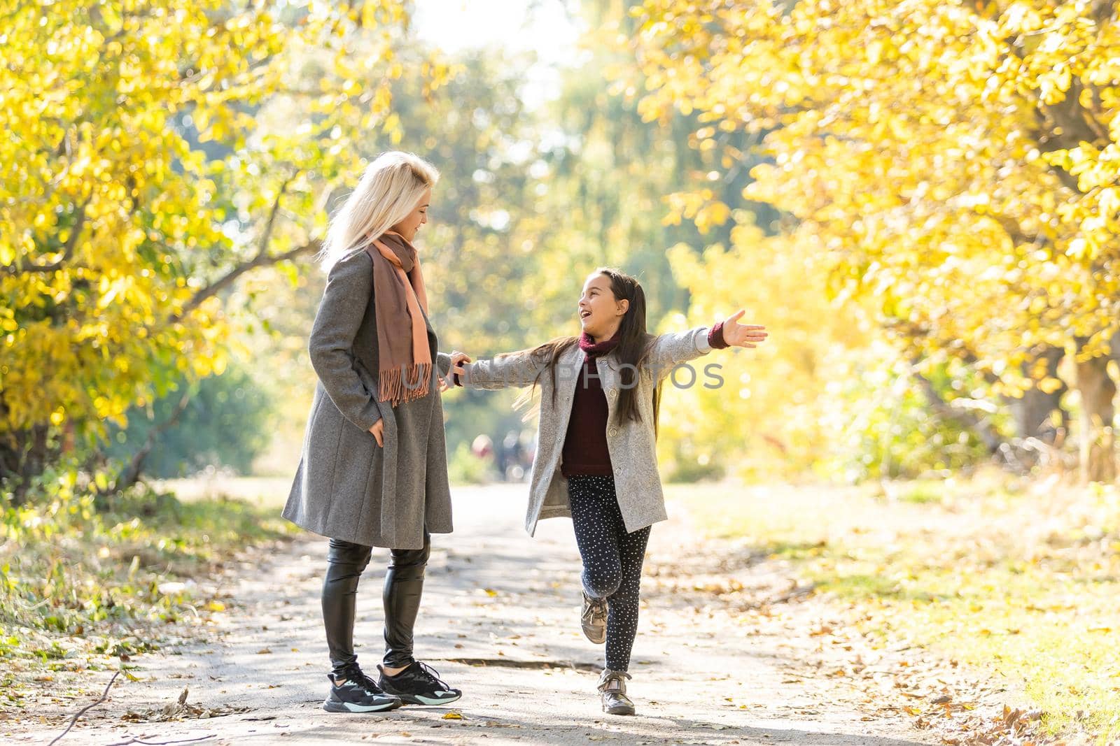 Little girl and her mother enjoy sunny weather in the autumn park by Andelov13
