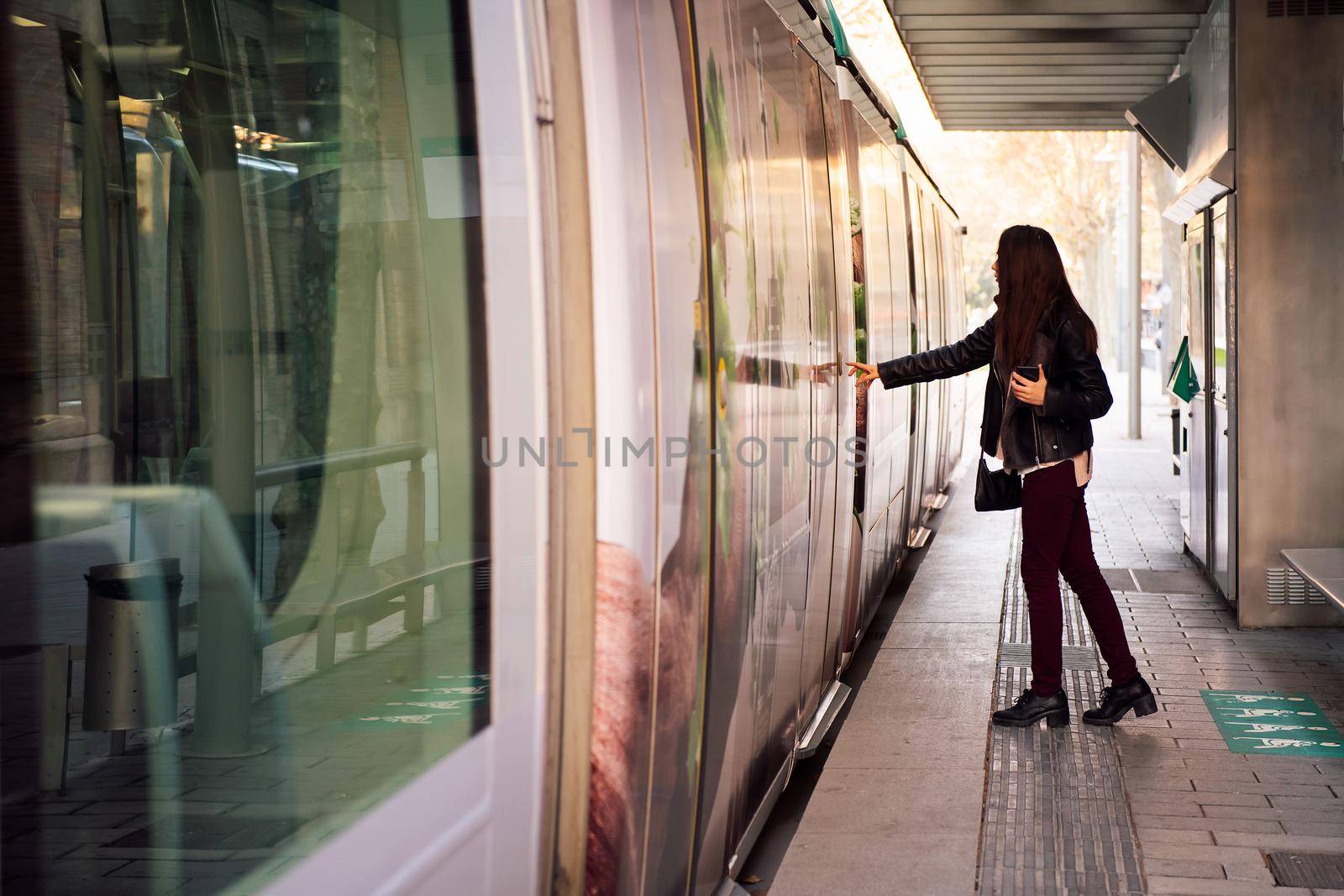 young woman pressing the door button to open the door and board the streetcar, concept of public transportation and urban lifestyle