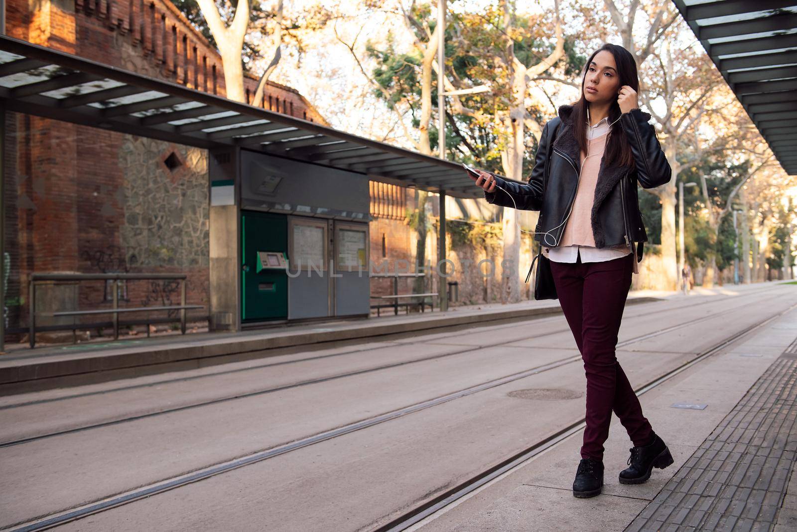 woman putting on her telephone earphones at the streetcar stop, concept of technology and communication, copyspace for text