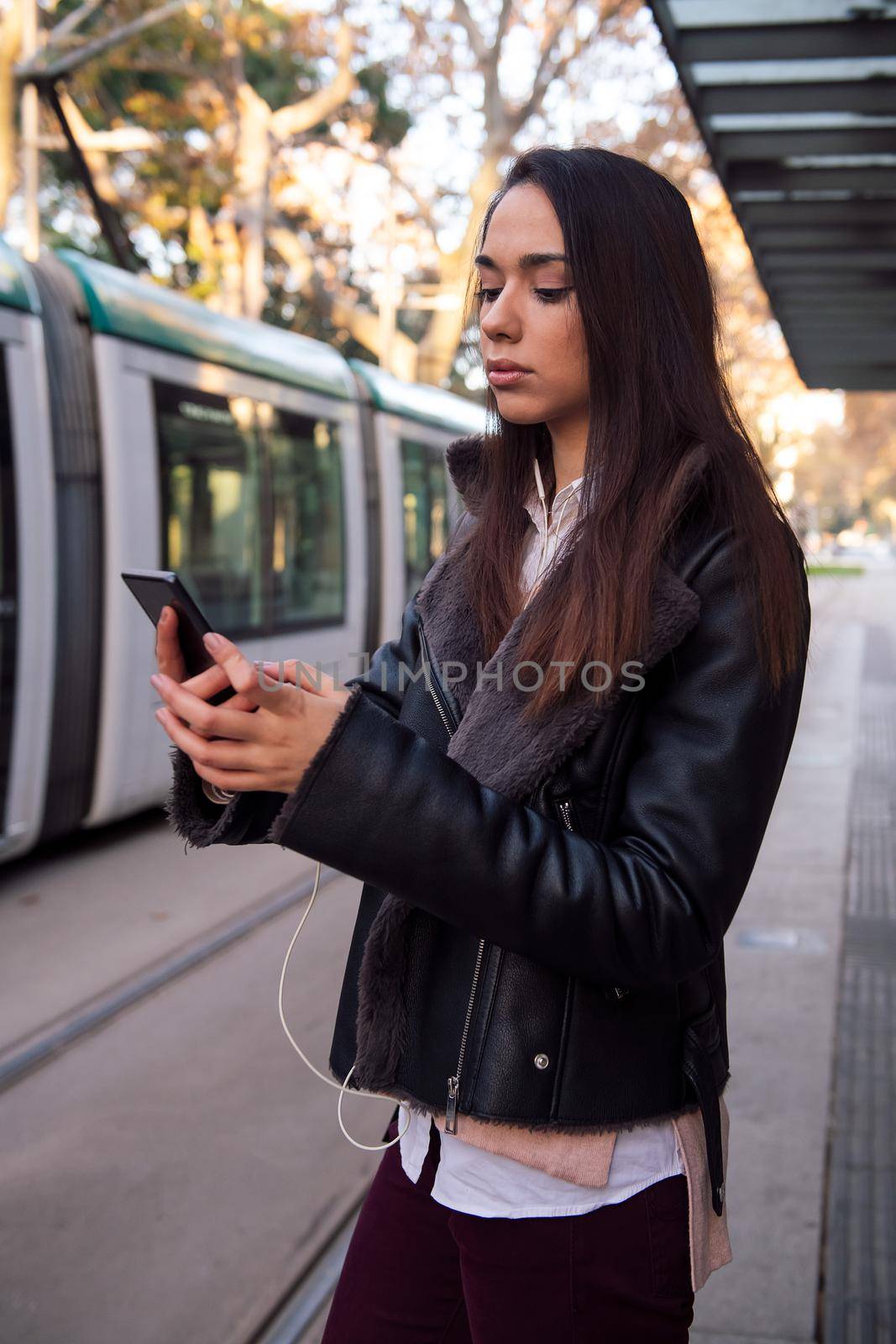woman consulting her telephone at the streetcar stop by raulmelldo