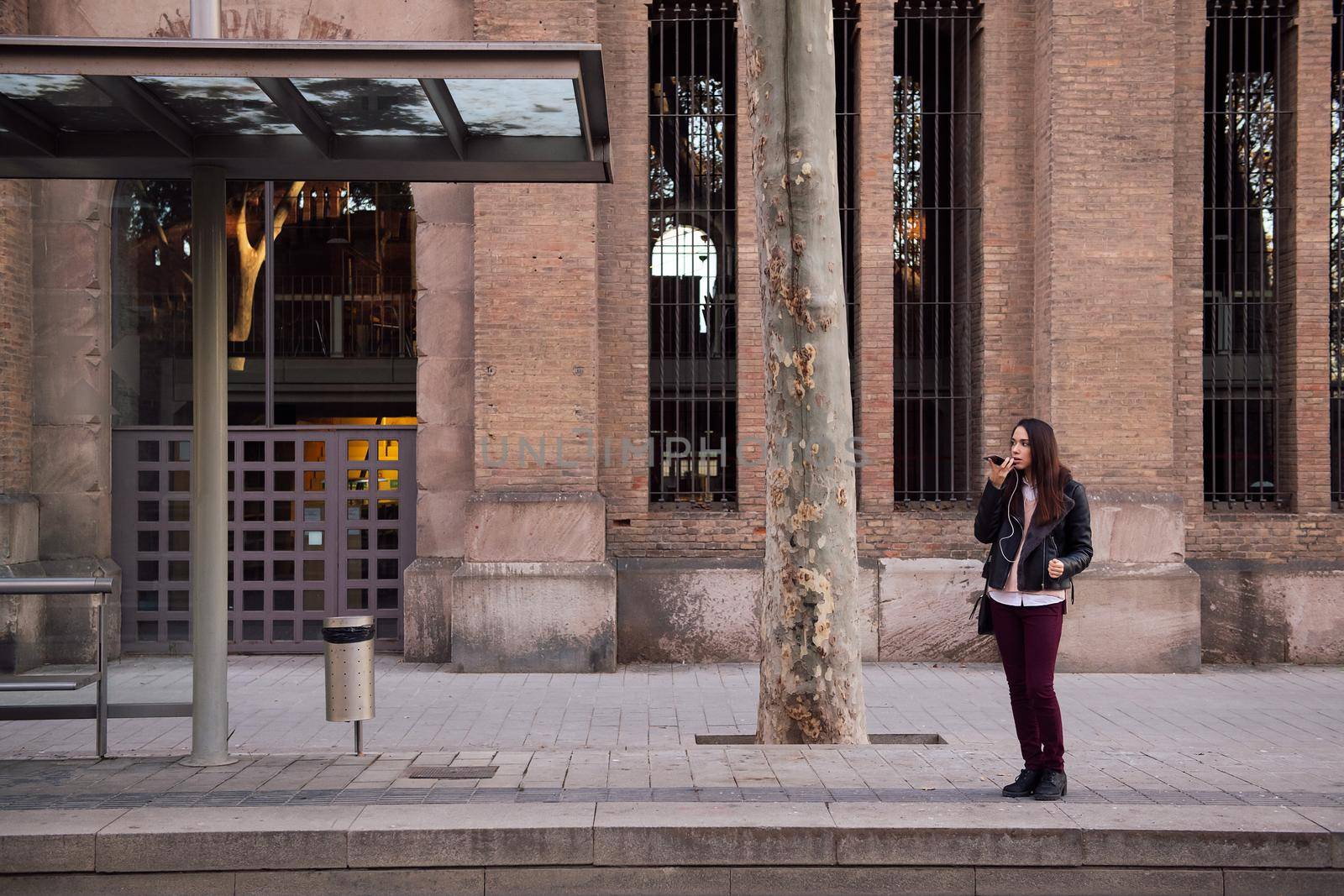 woman recording a voice message with her telephone at the streetcar stop, concept of technology and communication, copyspace for text