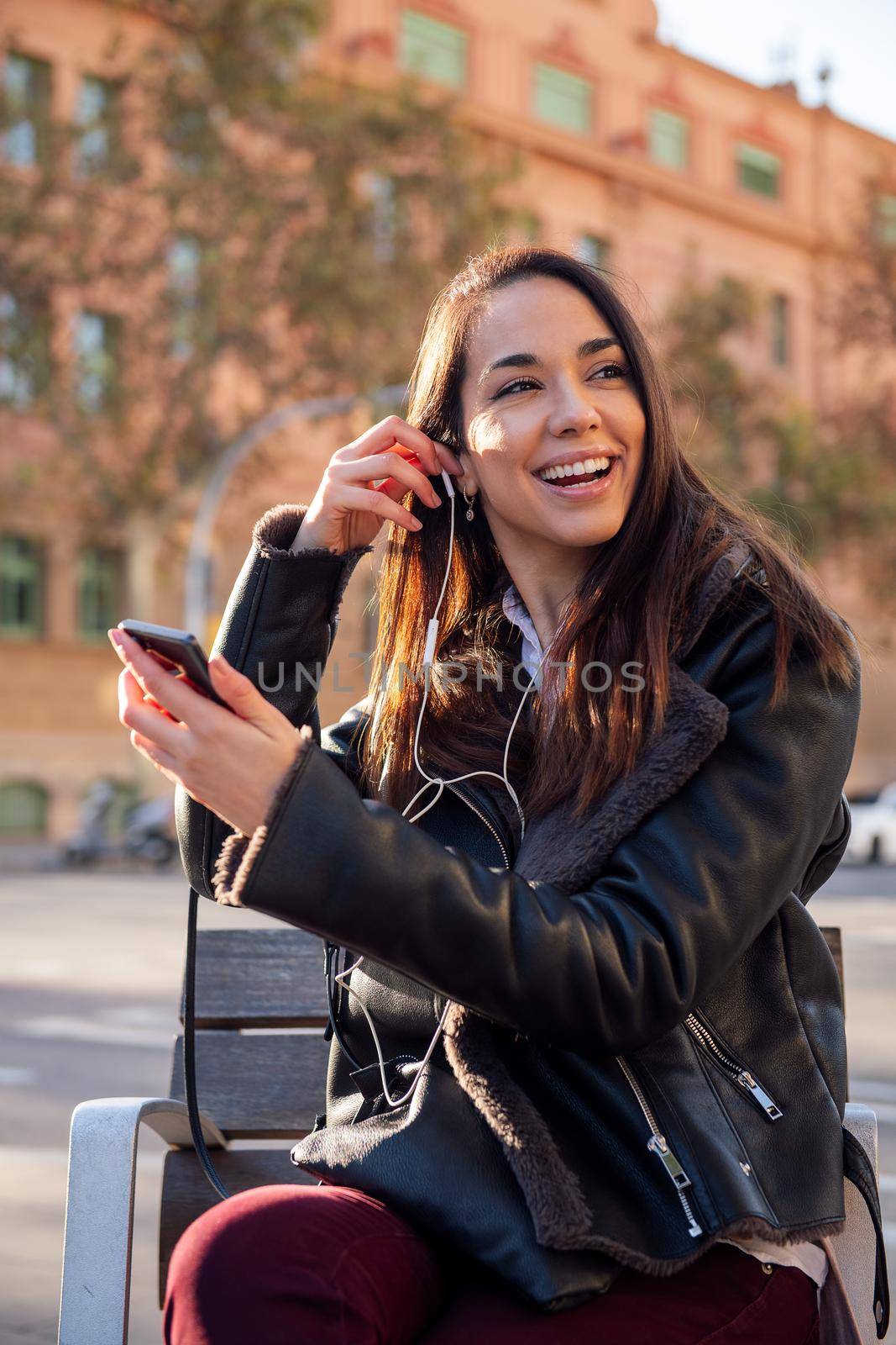 vertical portrait of a happy woman putting on the earphones of her phone, concept of communication and urban lifestyle, copyspace for text