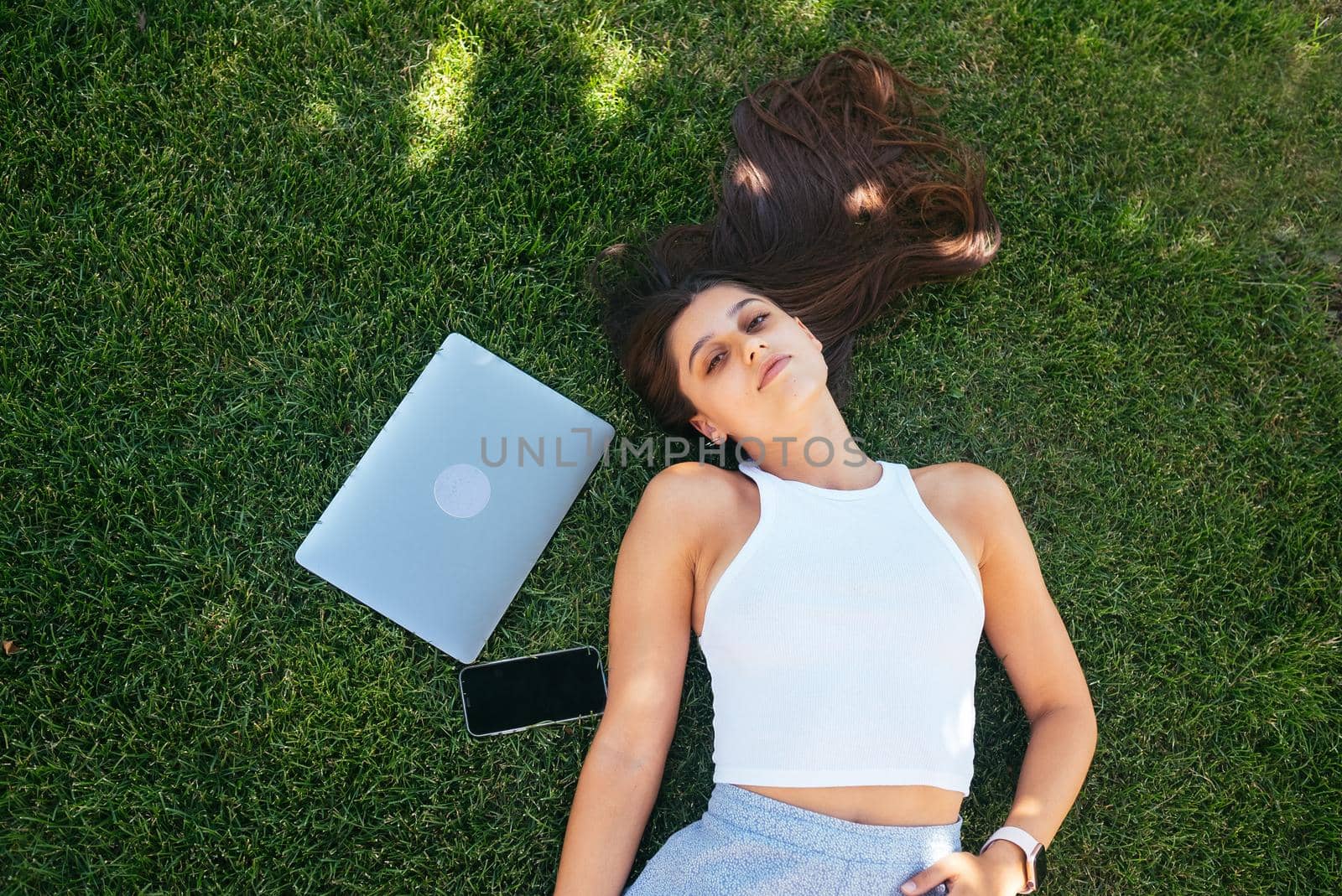 Young fit attractive woman lying on green lawn park. Perks of freelance concept. Background, copy space