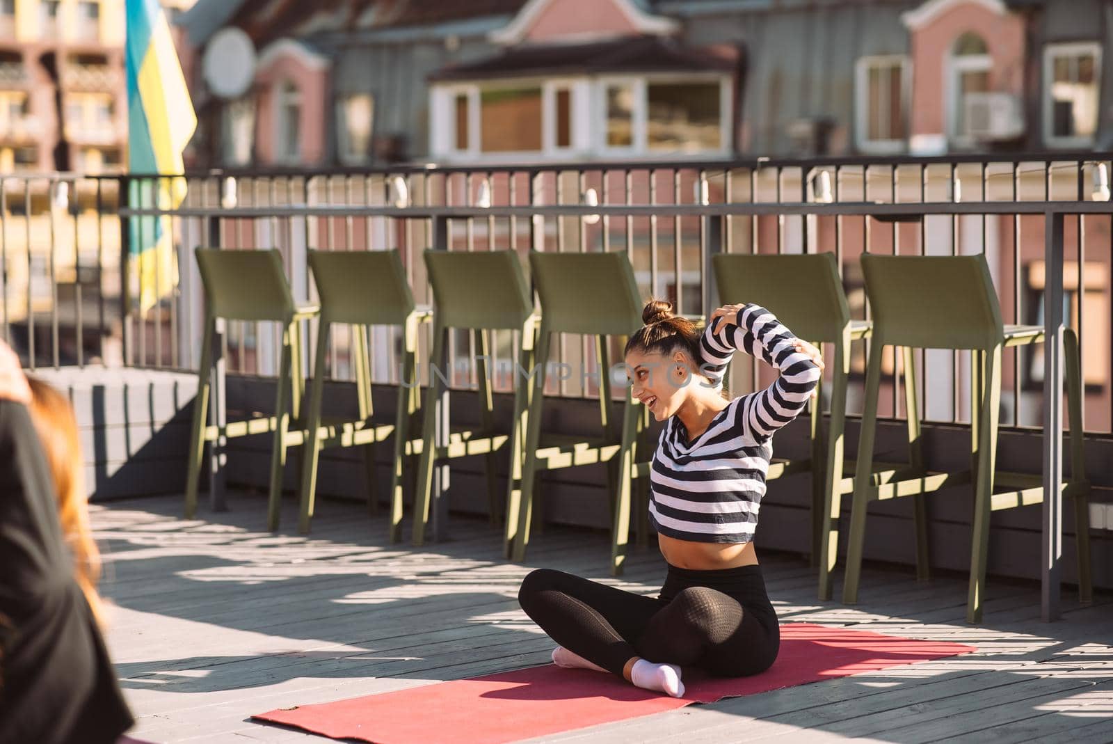 Yogi woman and diverse group of young sporty people practicing yoga, female students training at house's roof. Well being, wellness concept