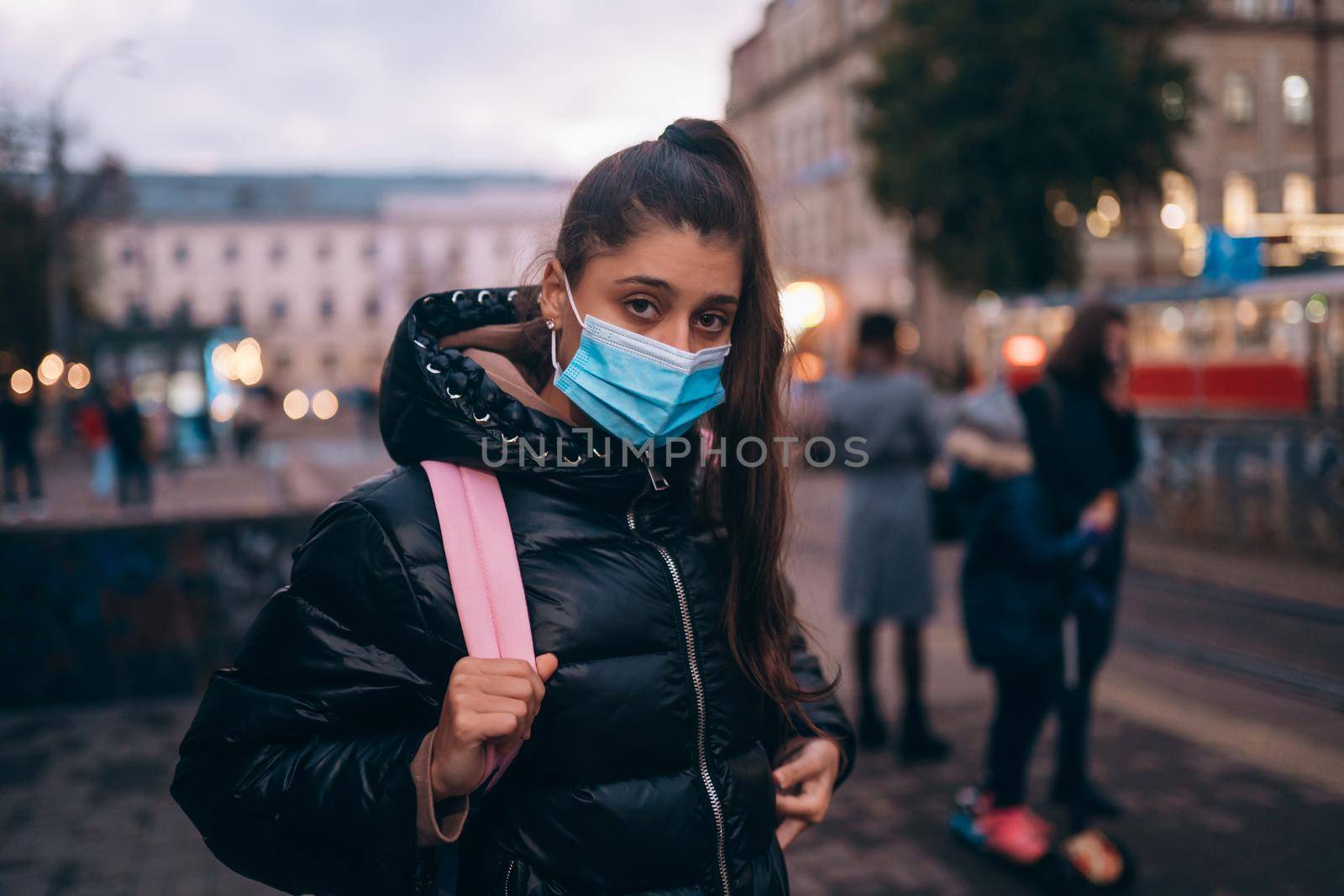 Portrait of beautiful young student woman in medical mask posing outdoors with a backpack