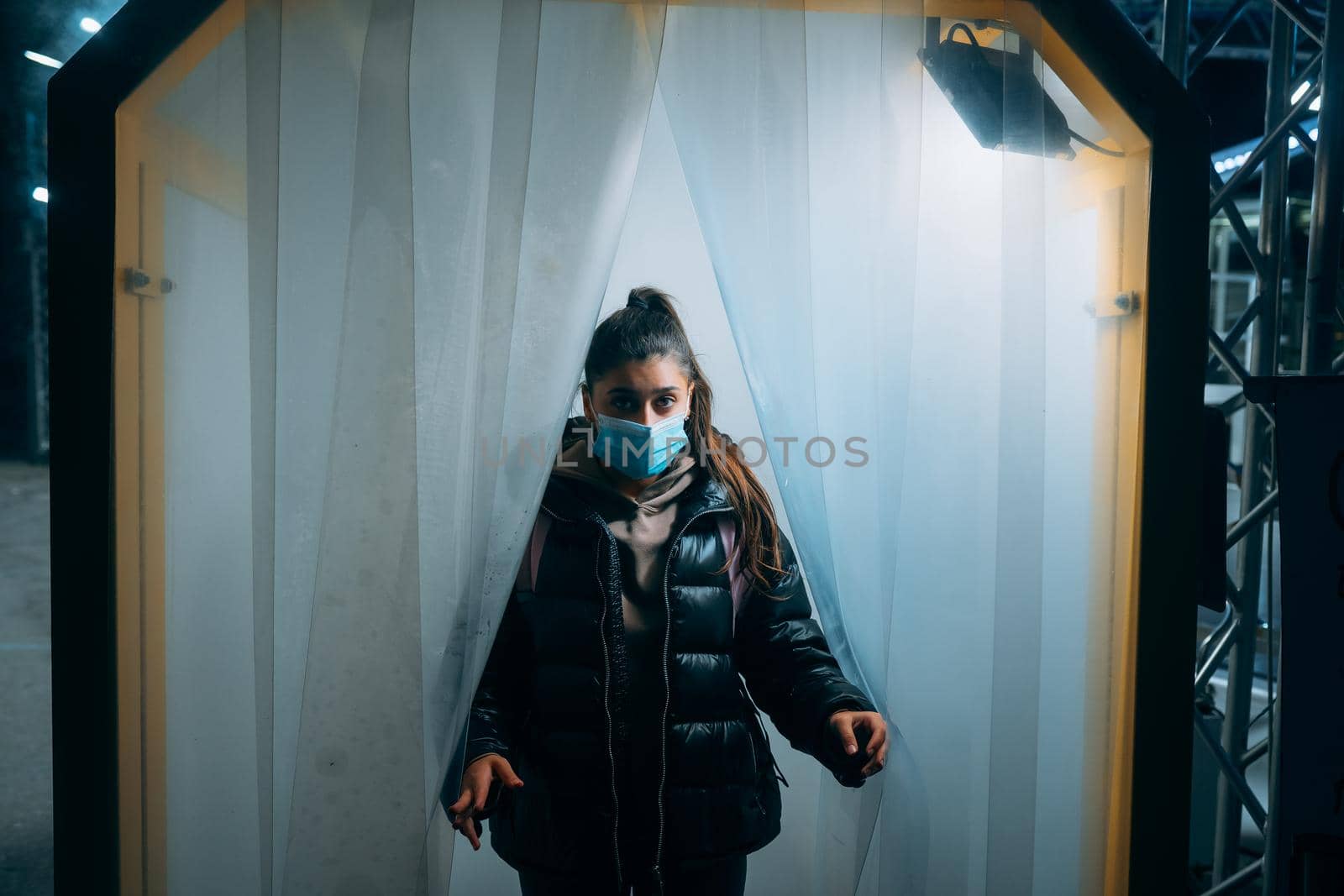 Young beautiful woman in a medic mask is staying in a disinfection tunnel