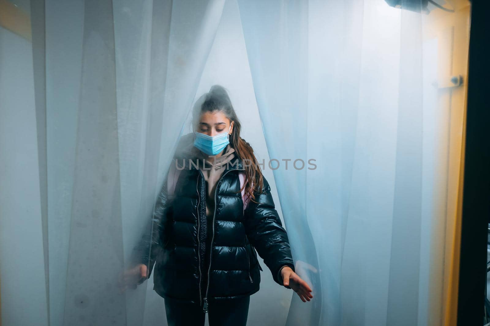 Young beautiful woman in a medic mask is staying in a disinfection tunnel