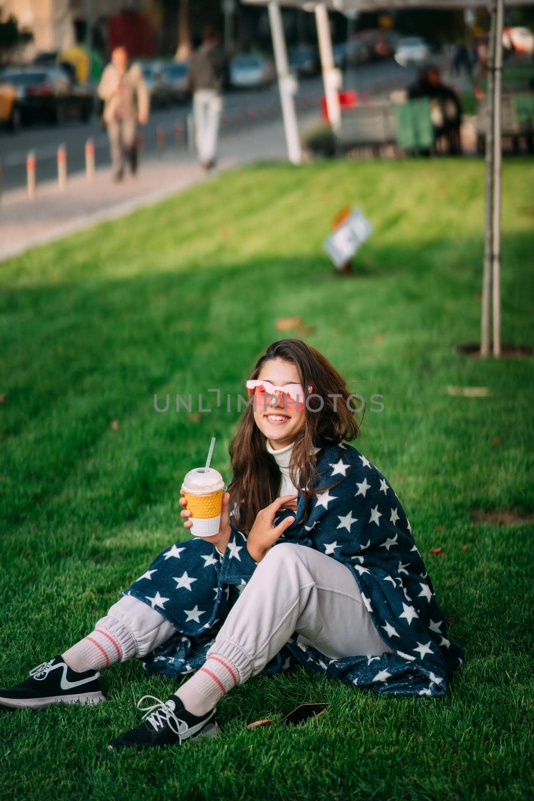 portrait of a young attractive woman in the park with a paper glass of coffee. Rest in the park