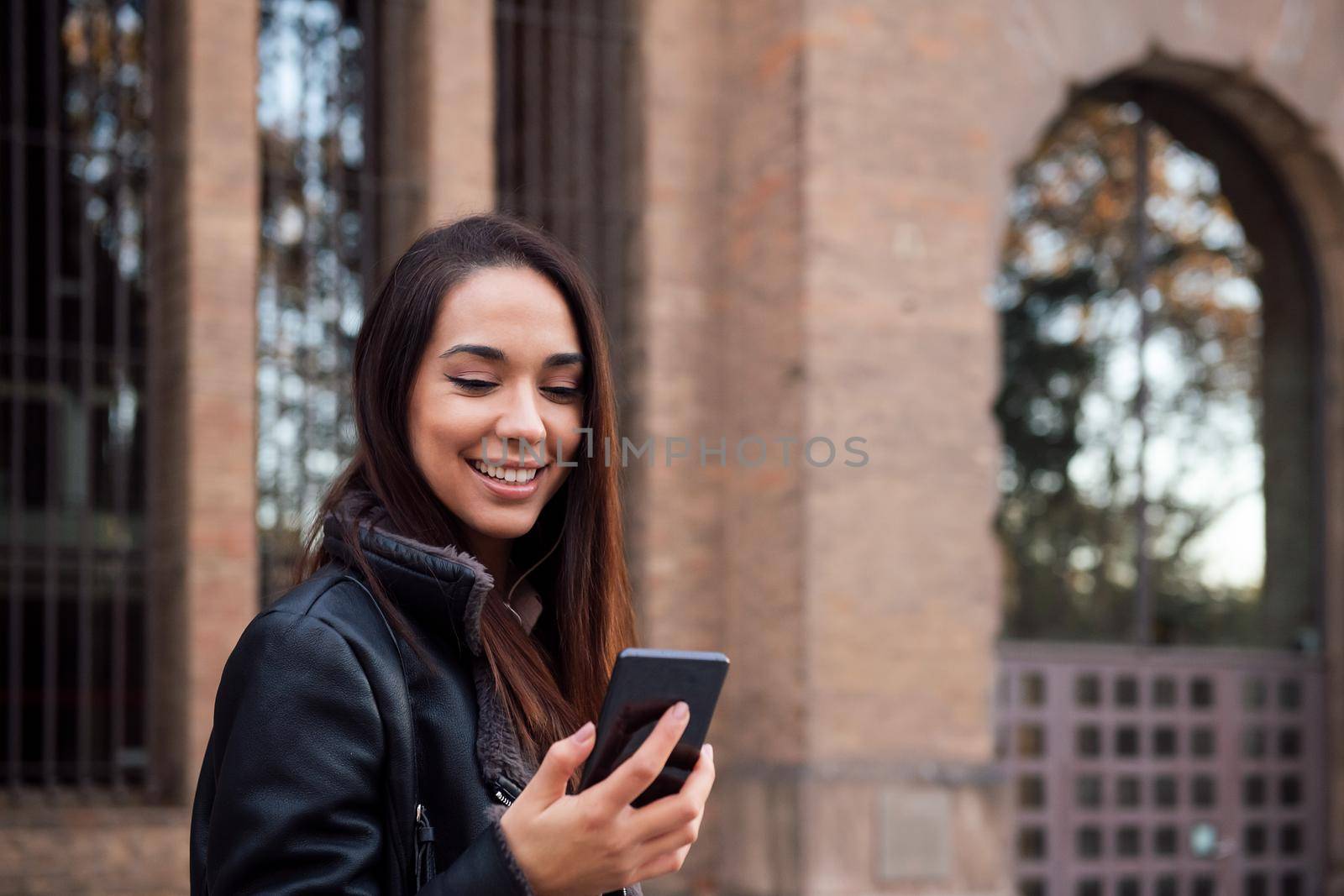 smiling young woman looking at her telephone at the street, concept of technology and communication, copyspace for text
