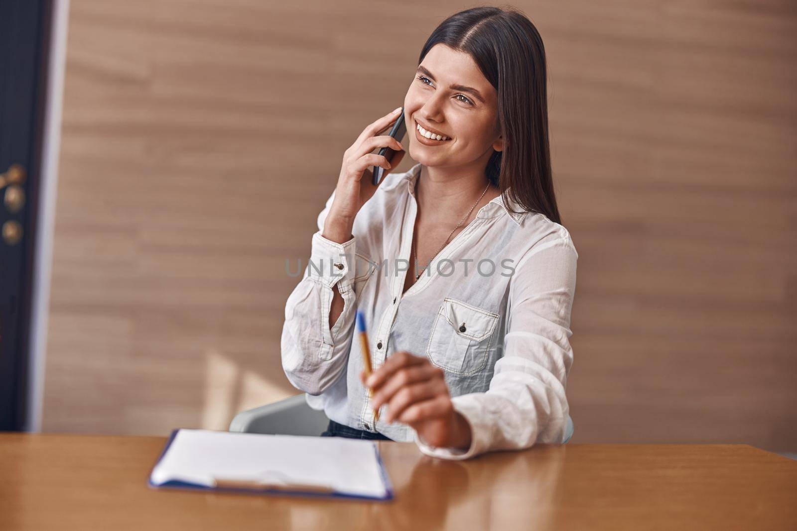 Happy smiling caucasian woman with phone and documents in modern clinic reception by Yaroslav_astakhov