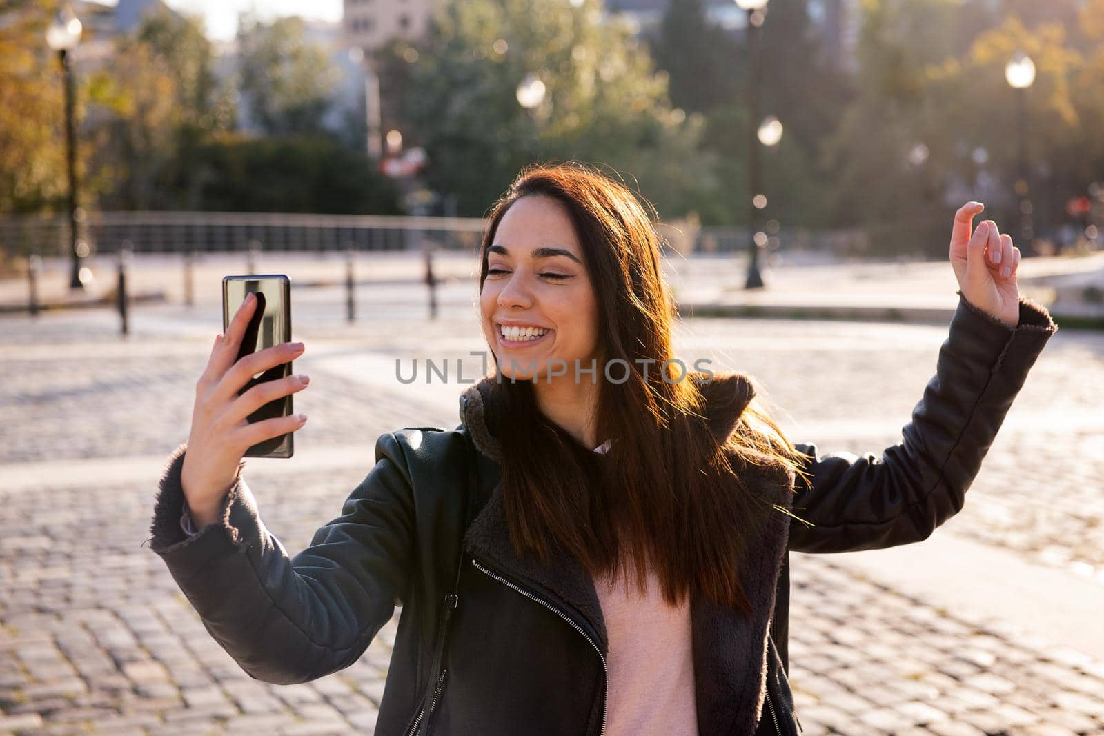 happy young woman smiling and celebrating looking the phone on a cobblestone street, concept of technology and urban lifestyle, copyspace for text
