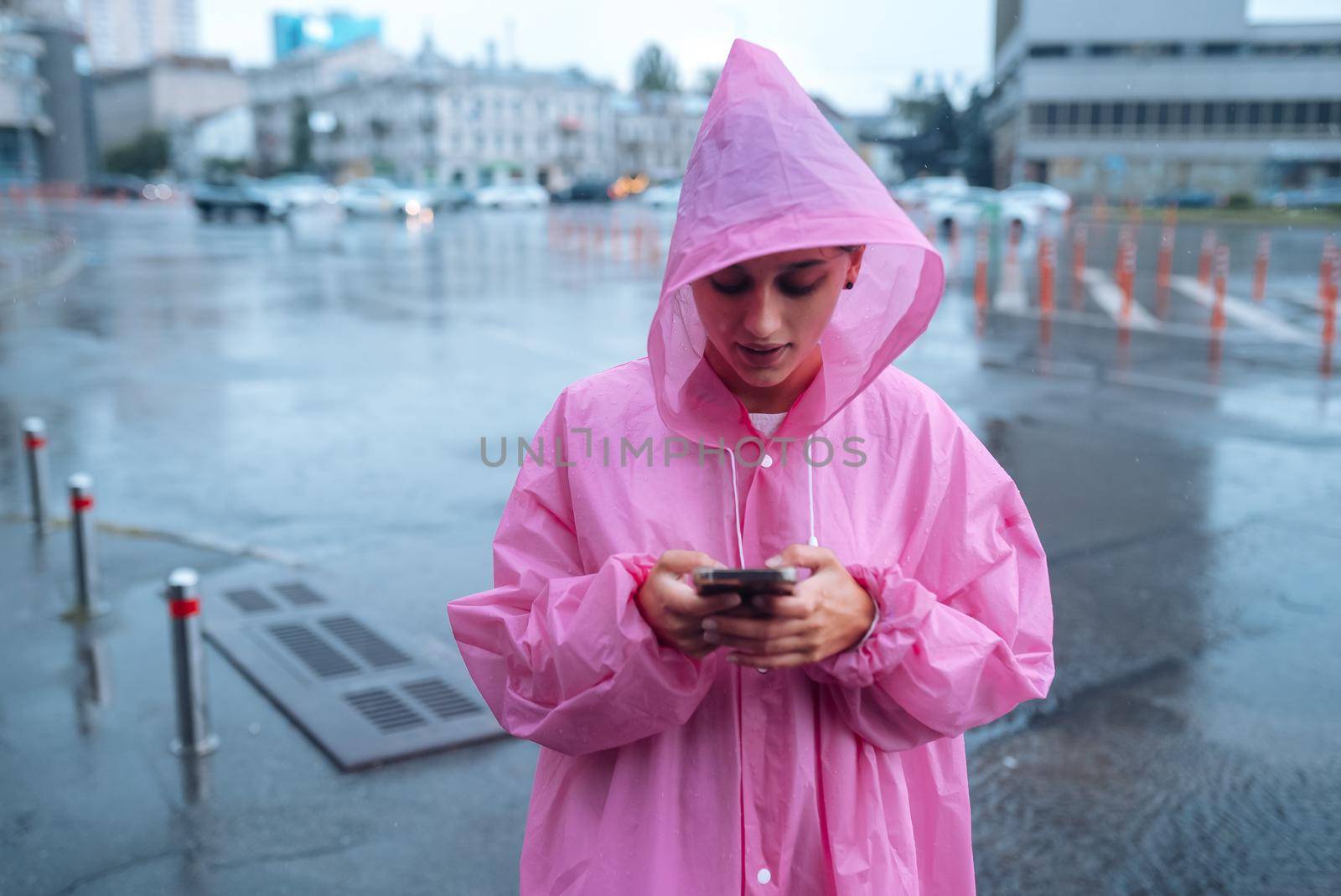 A young woman in a raincoat is waiting for someone in the rain