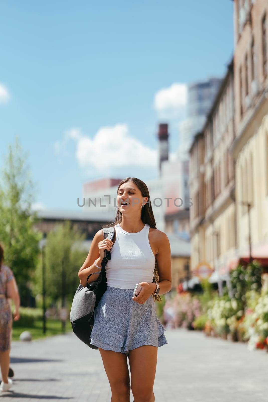Urban young hipster woman with stylish backpack walks around the city near a building in the spring day. Pretty girl travels.