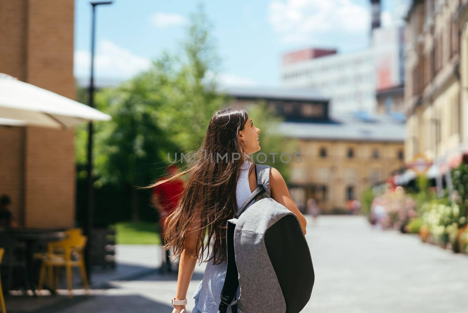 Urban young hipster woman with stylish backpack walks around the city near a building in the spring day. Pretty girl travels.