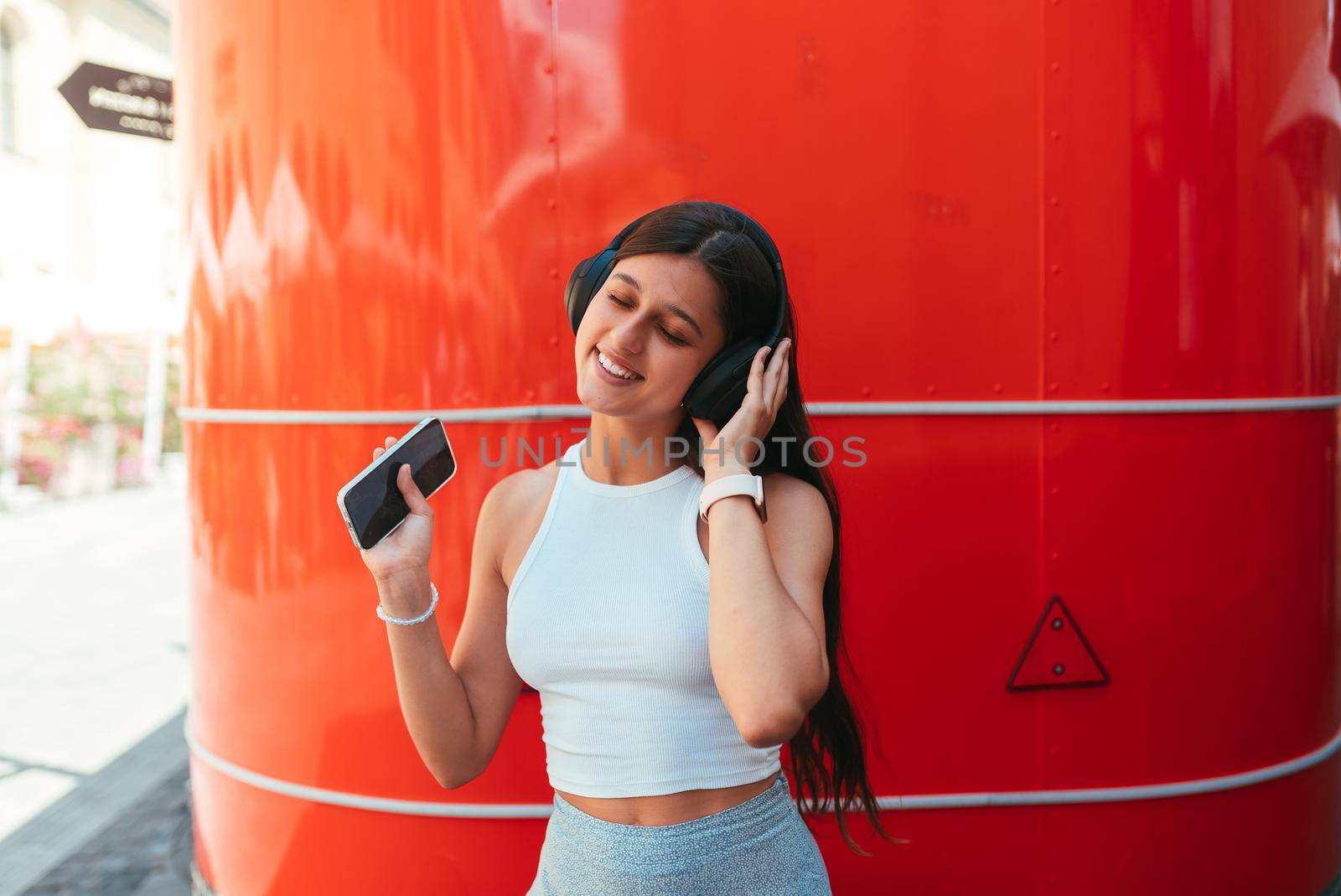 Portrait of a happy girl listening music online with wireless headphones from a smartphone in the street