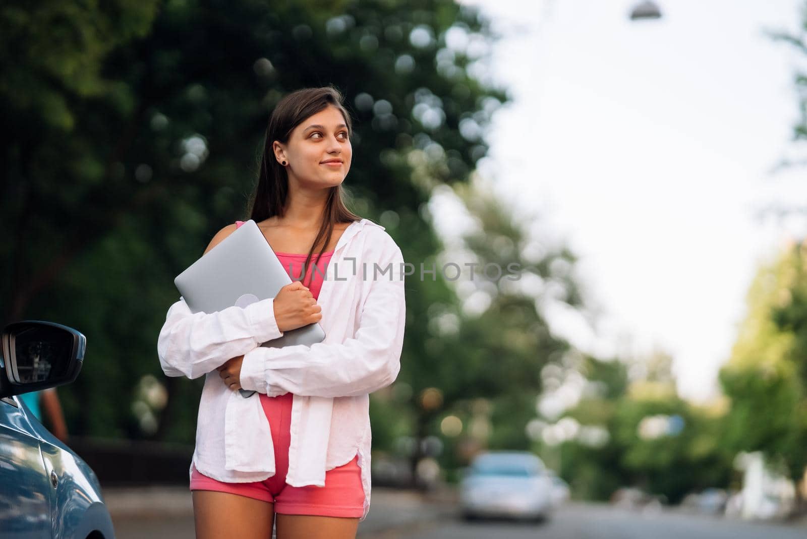 Image of young cheerful beautiful woman walking outdoors holding laptop computer
