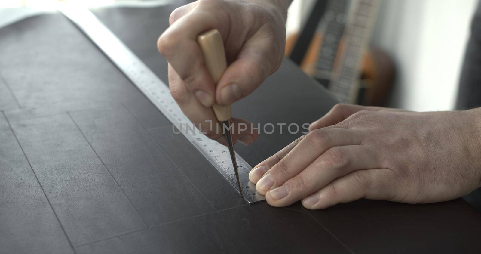 Close up of leather craftsman working with natural leather by awl and ruler. Handmade master at work in local workshop. Leather wallet stitch