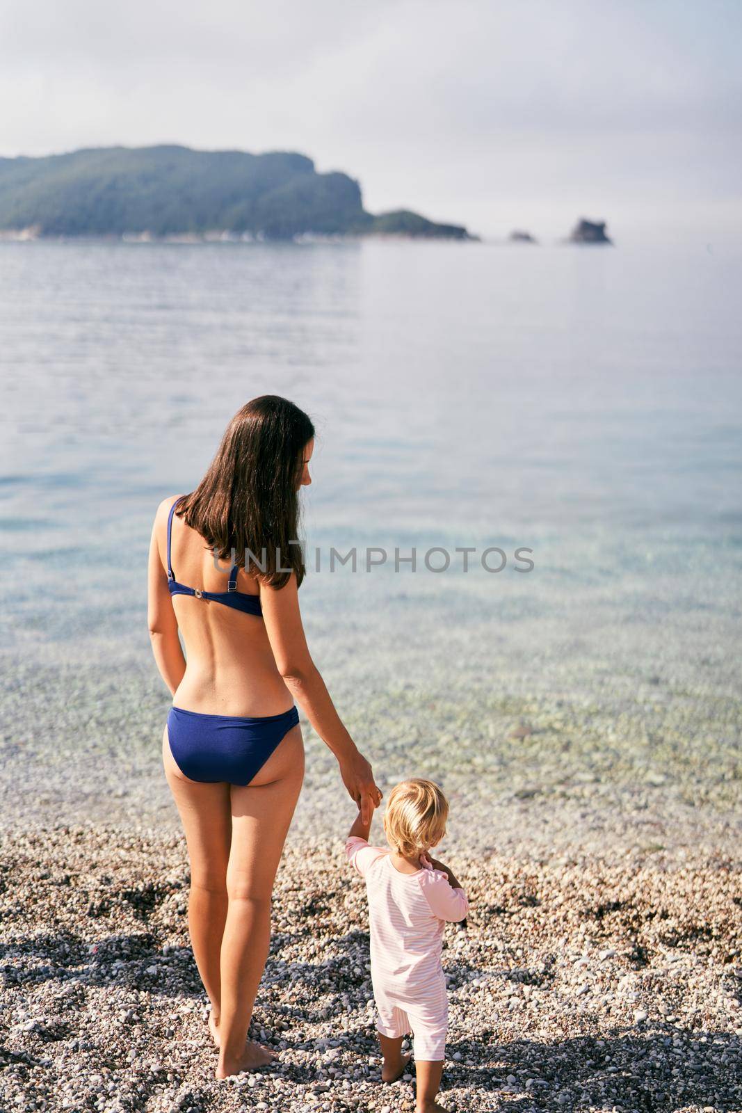 Mom stands with a little girl on the beach near the water. High quality photo