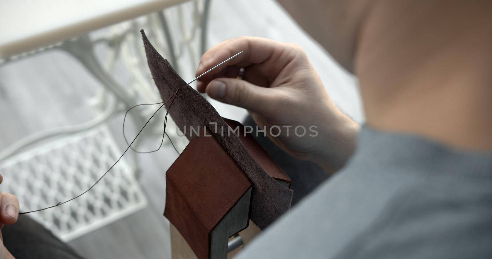 Craftsman sewing a handmade brown leather wallet in workshop. by vovsht