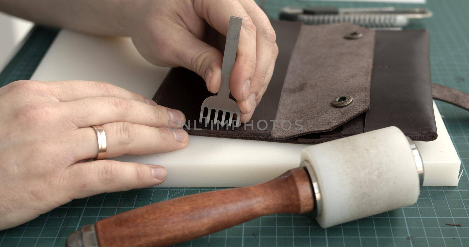 Punching holes in the leather with a hole punch with a hammer. Craftsman making holes in leather with puncher tool. Sewing wallet