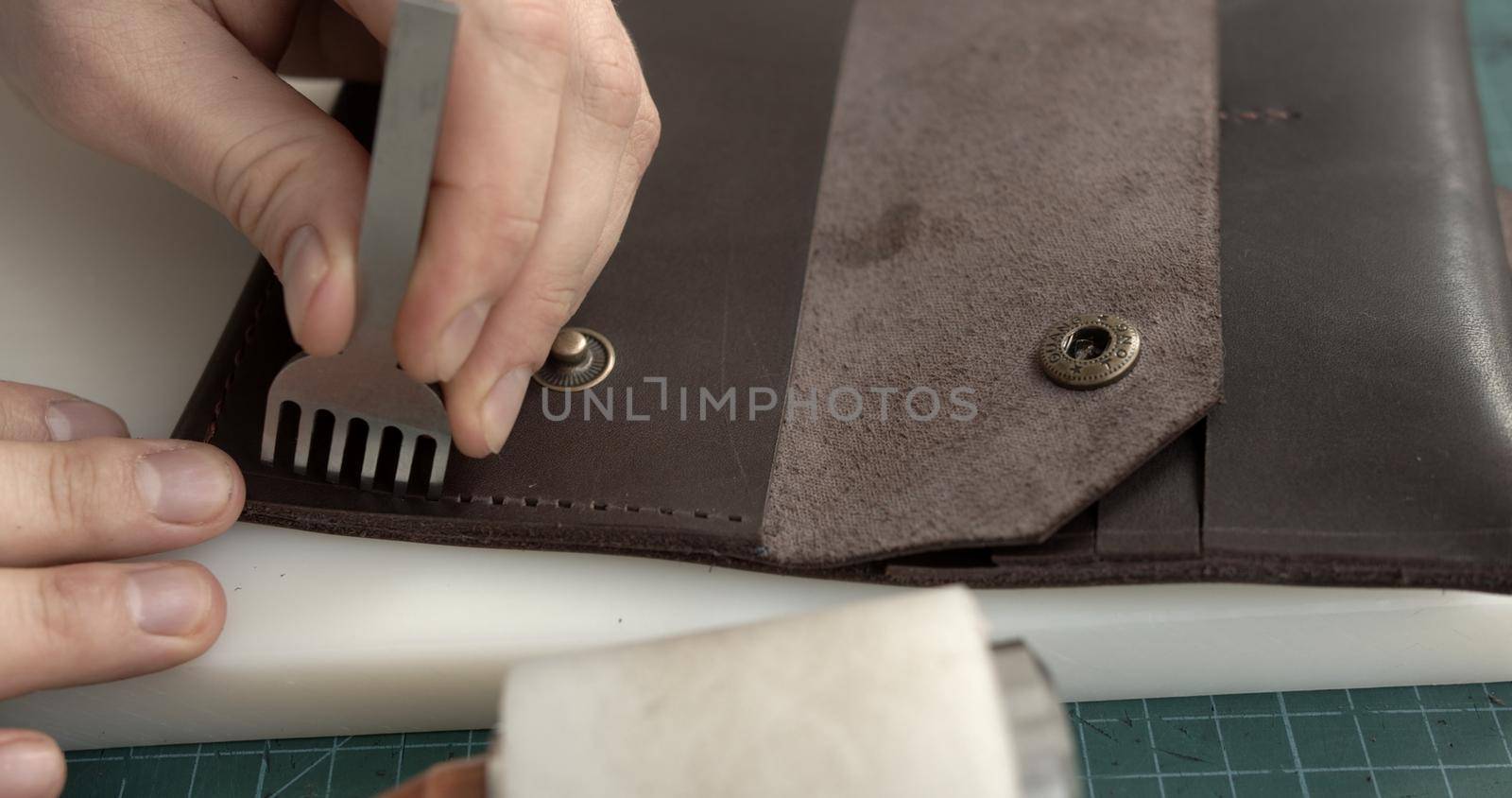 A man makes a handmade leather wallet from genuine leather. by vovsht