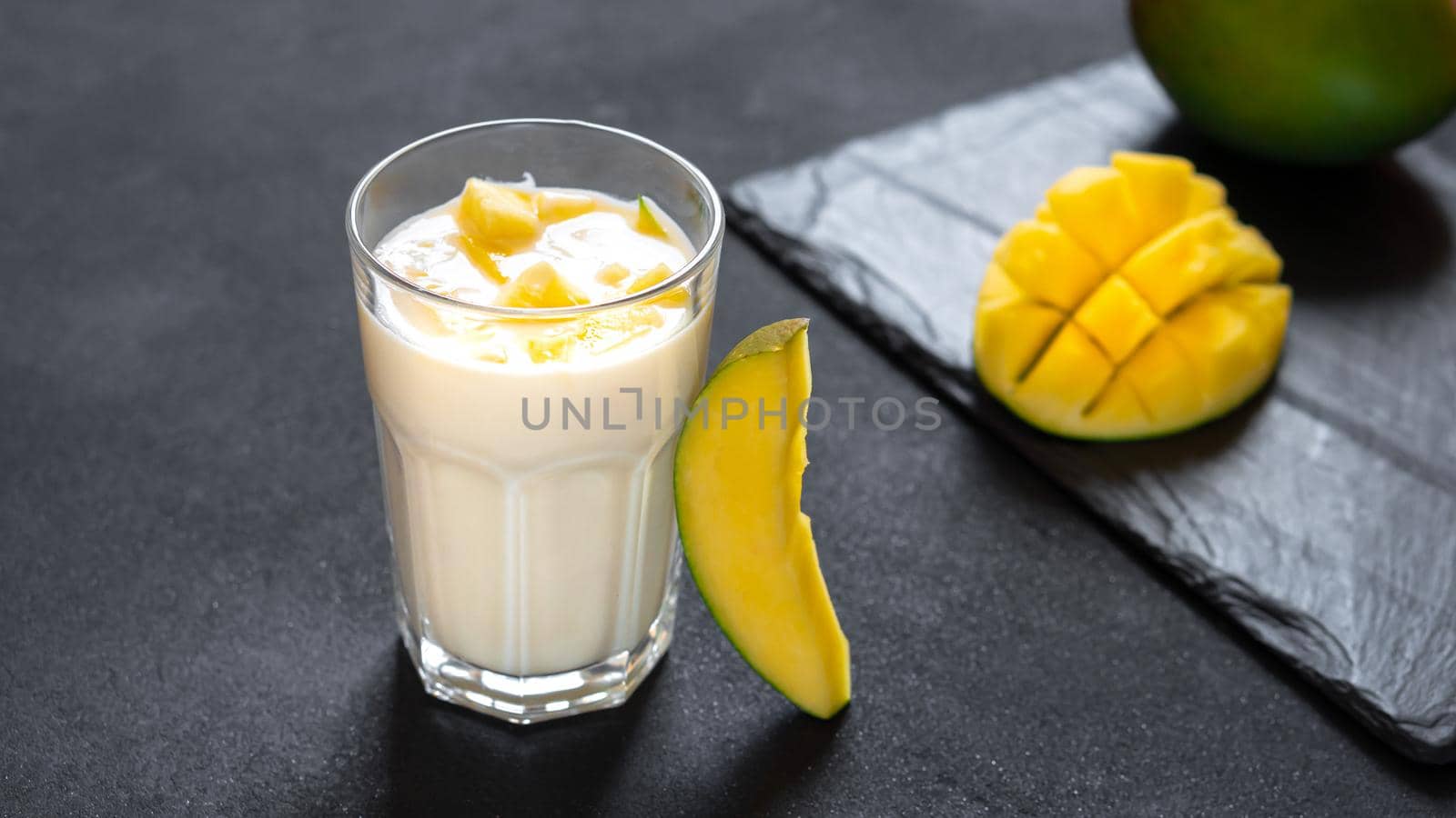 Lassi is a popular traditional dahi, yogurt based cold drink in India. Lassi consists of yogurt, water, spices and sometimes fruit and ice. Milk shake on black background with mango pieces