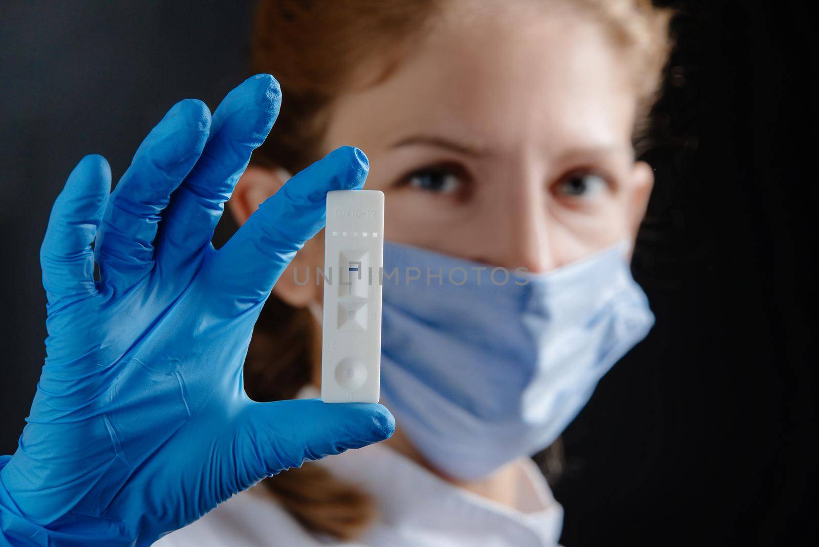 A female doctor or nurse is holding a covid test 19. Physician with test in hand and blue protective medical gloves on black background