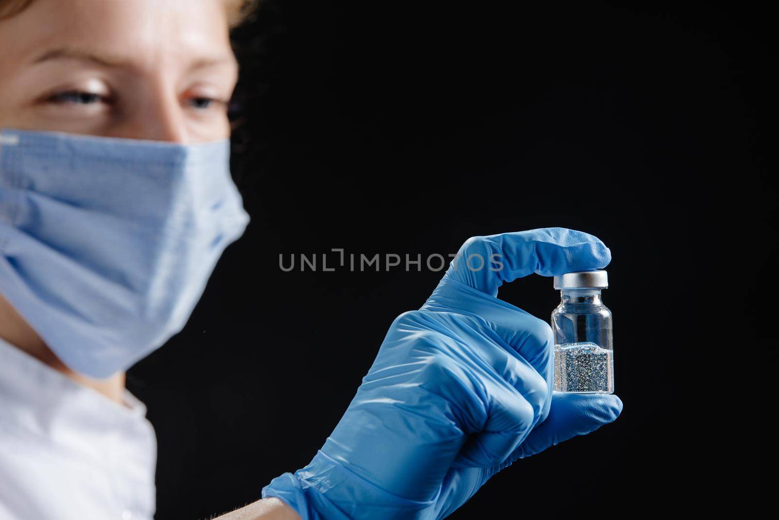 A woman doctor is holding a tube of medicine against a black background. Nurse holding medicine.