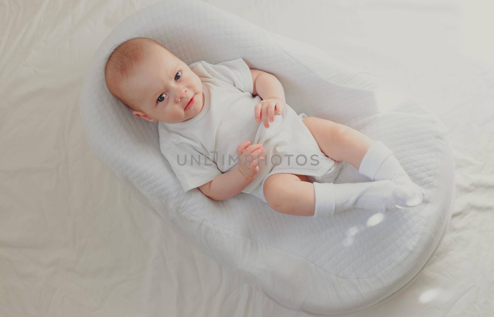 The baby is lying in a cocoon of copy space . The baby is 0-3 months old. A contented infant. An article about choosing a cocoon for newborns. An article about the benefits of cocoon. An article about colic . White background. by alenka2194