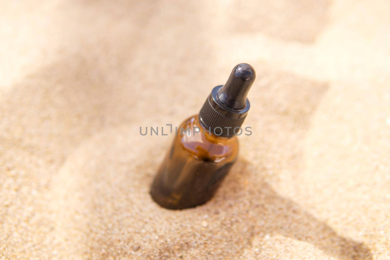 Cosmetic serum for the skin in a glass bottle. A bottle with a pipette on a sandy beach by the sea. Essences for skin care on a sandy background. The concept of natural cosmetics and SPA products.