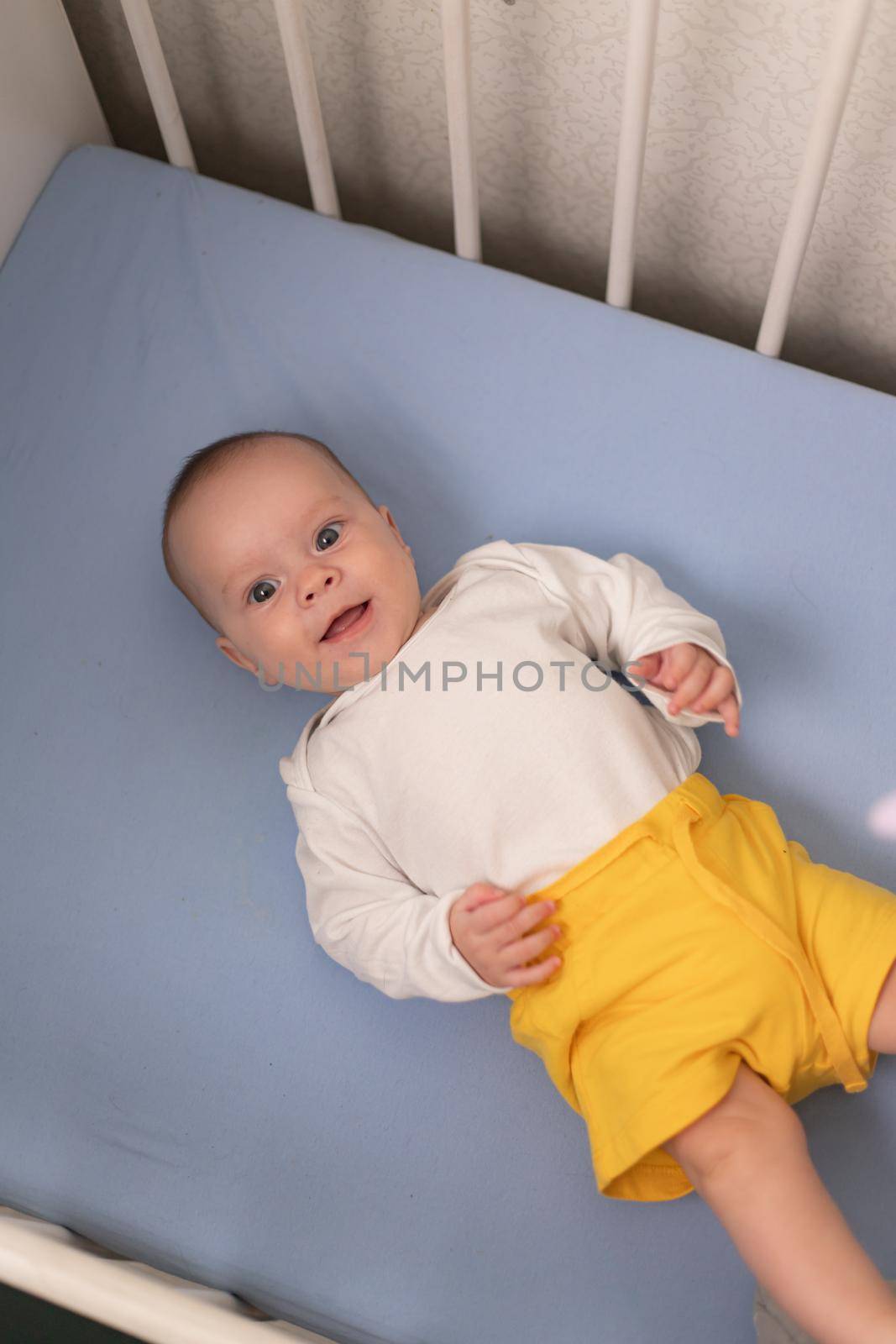 The baby is lying in his crib and looking at the camera . A happy child. Children's article. by alenka2194